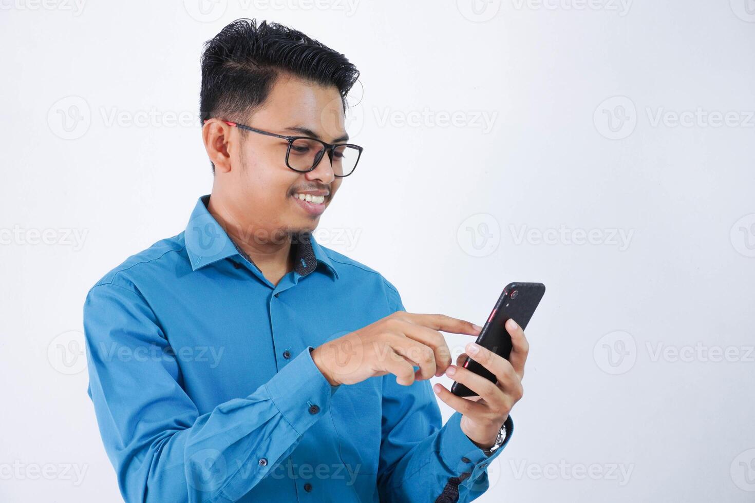 sorridente asiatico dipendente uomo con bicchieri Tenere e toccare il Telefono con dito indossare blu camicia isolato su bianca sfondo foto