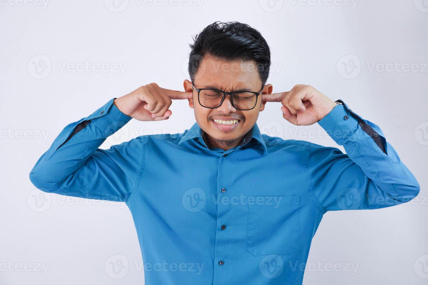 asiatico uomo d'affari coperto il suo orecchie con il suo dita con bicchieri indossare blu camicia isolato su bianca sfondo foto
