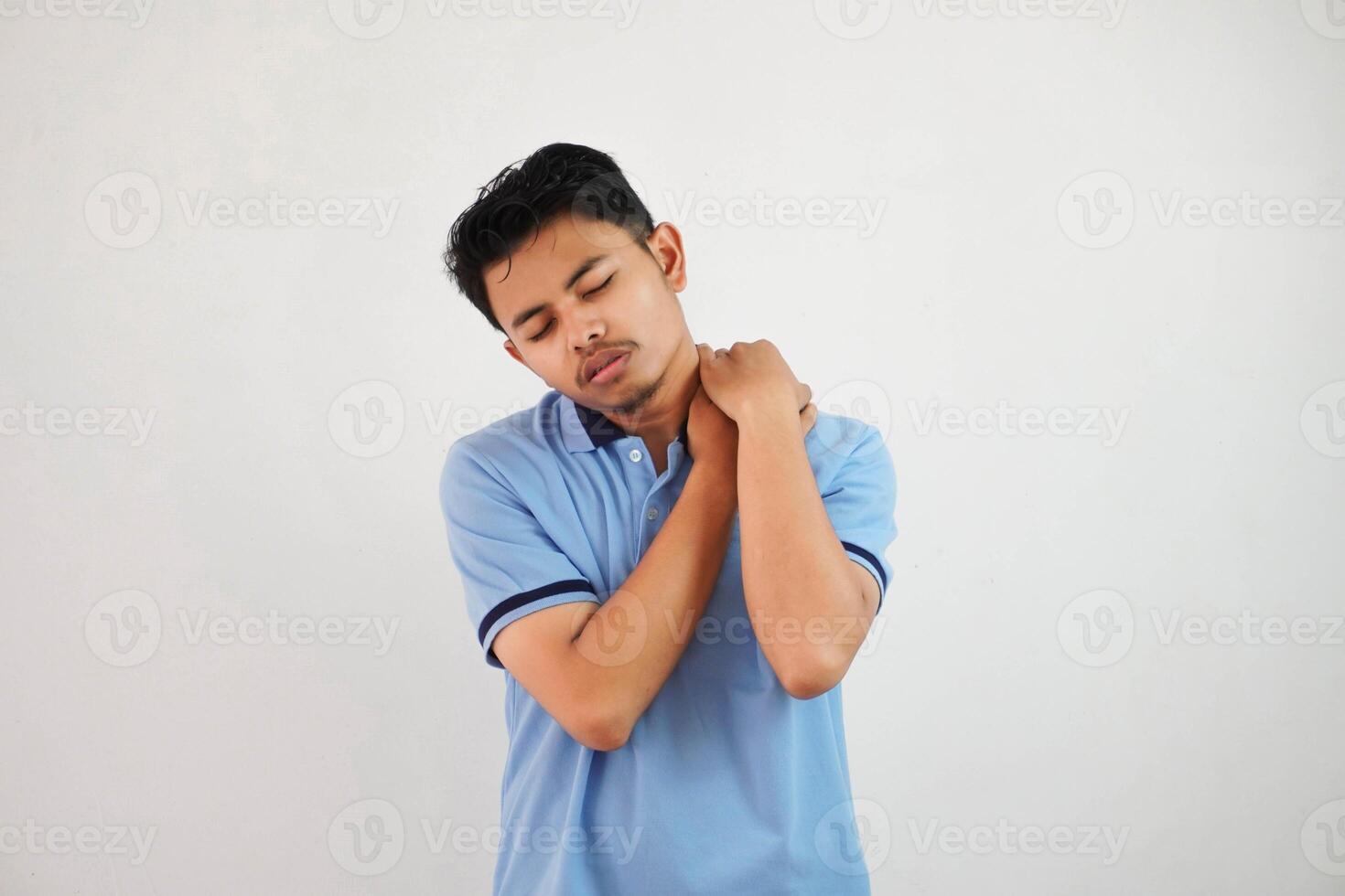 un' ritratto di giovane asiatico uomo avendo ha collo e spalla dolore indossare blu t camicia isolato su bianca sfondo foto