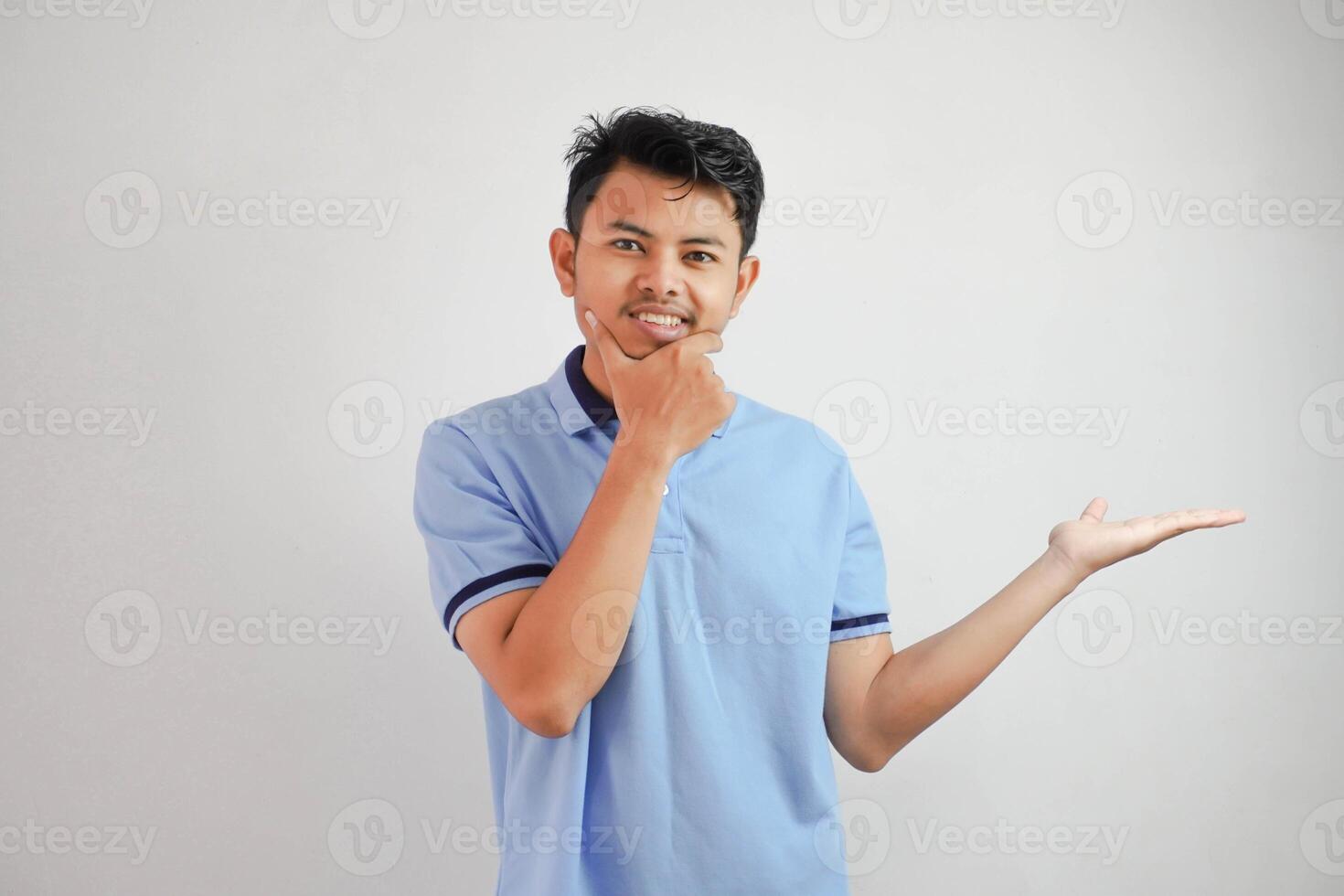 grave viso asiatico uomo con un Aperto mano il lato e mentre Tenere il mento indossare blu t camicia isolato su bianca sfondo foto