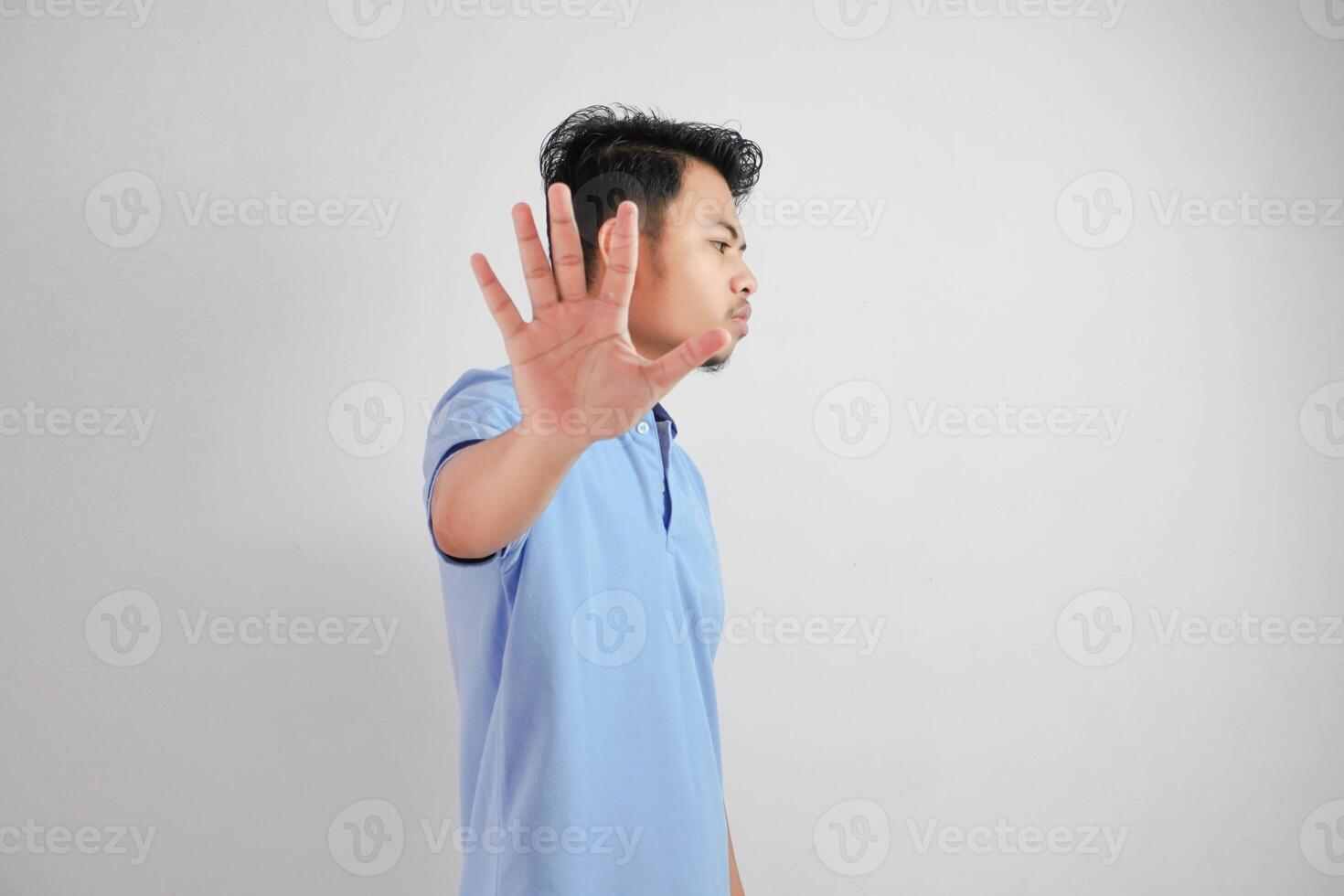 attraente asiatico uomo con mano gesto posa rifiuto o divieto mentre puntamento per copia spazio di il suo lato indossare blu t camicia isolato su bianca sfondo foto