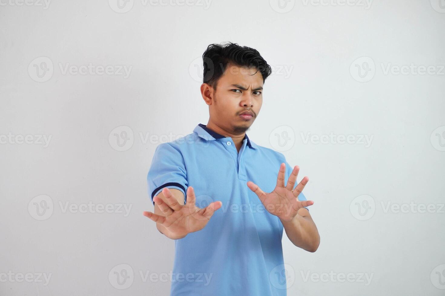 attraente asiatico uomo con mano gesto posa rifiuto o divieto mentre puntamento per copia spazio di il suo davanti indossare blu t camicia isolato su bianca sfondo foto