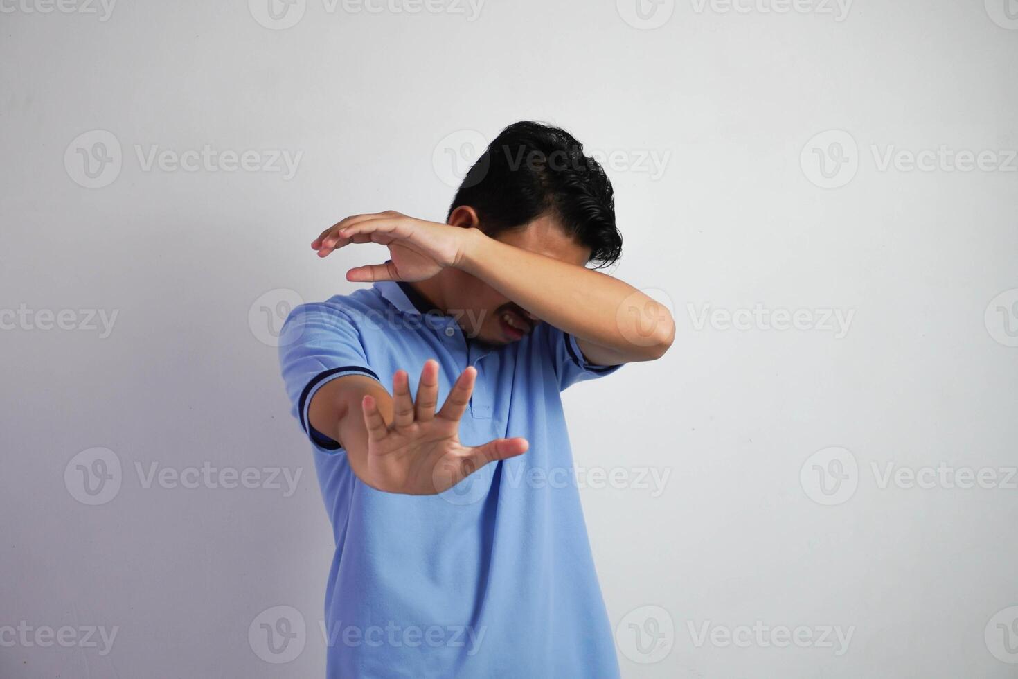 attraente asiatico uomo con mano gesto posa rifiuto o divieto mentre puntamento per copia spazio di il suo lato indossare blu t camicia isolato su bianca sfondo foto