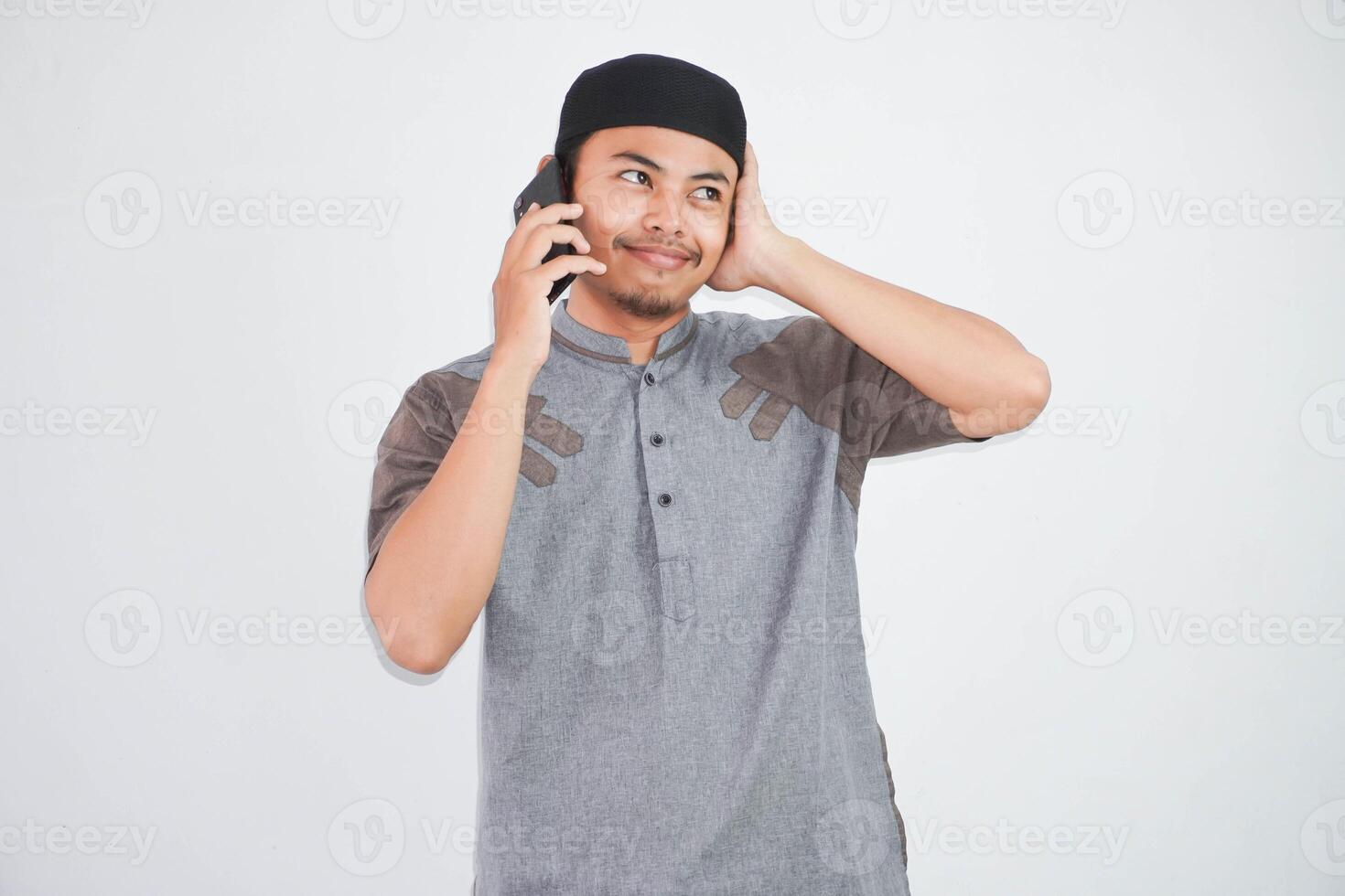 confuso giovane asiatico musulmano uomo parlando su mobile Telefono con mani Tenere testa indossare grigio musulmano Abiti isolato su bianca sfondo foto