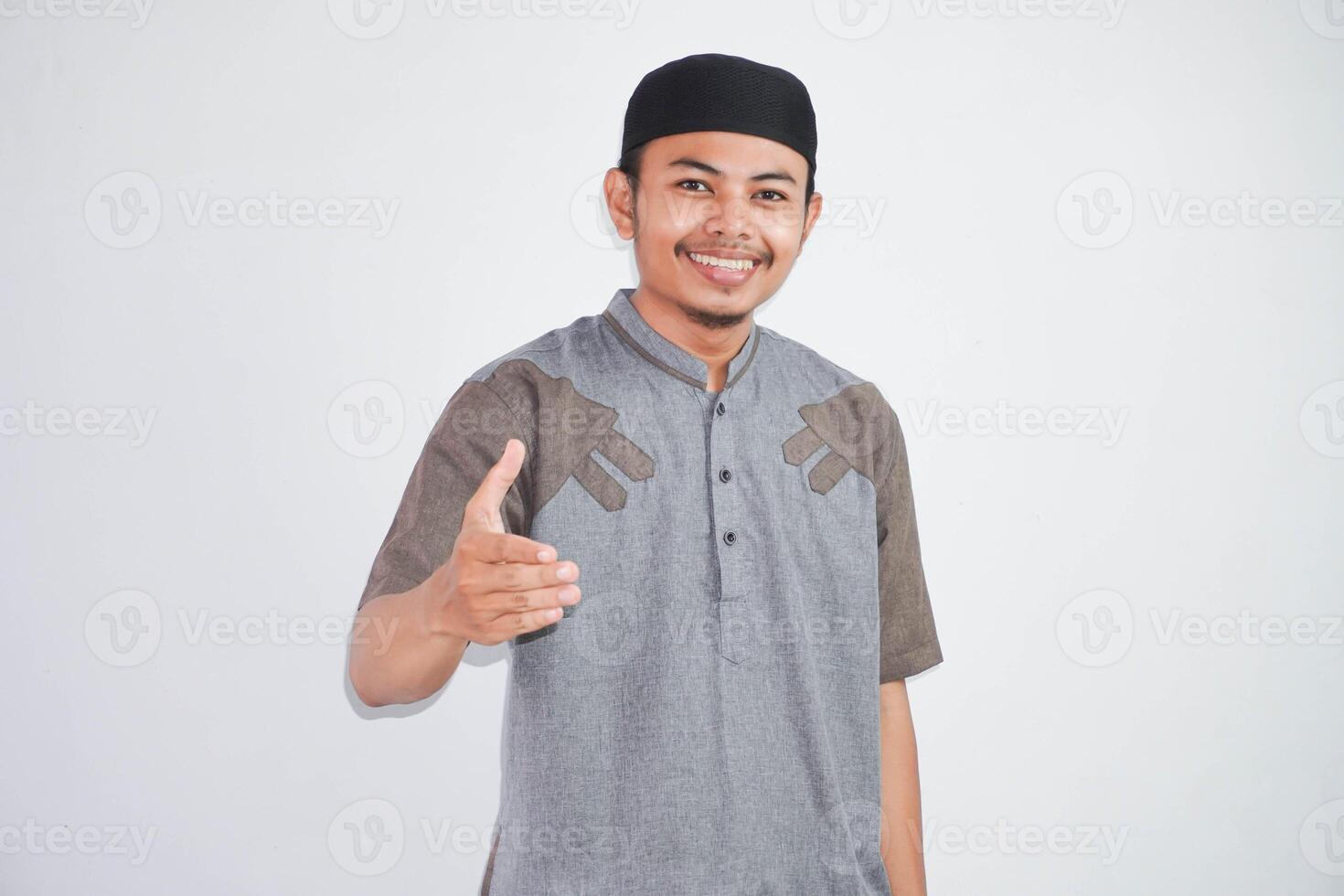 sorridente asiatico musulmano uomo amichevole offerta stretta di mano come saluto e accogliente. riuscito affari.indossare grigio koko Abiti isolato su bianca sfondo foto