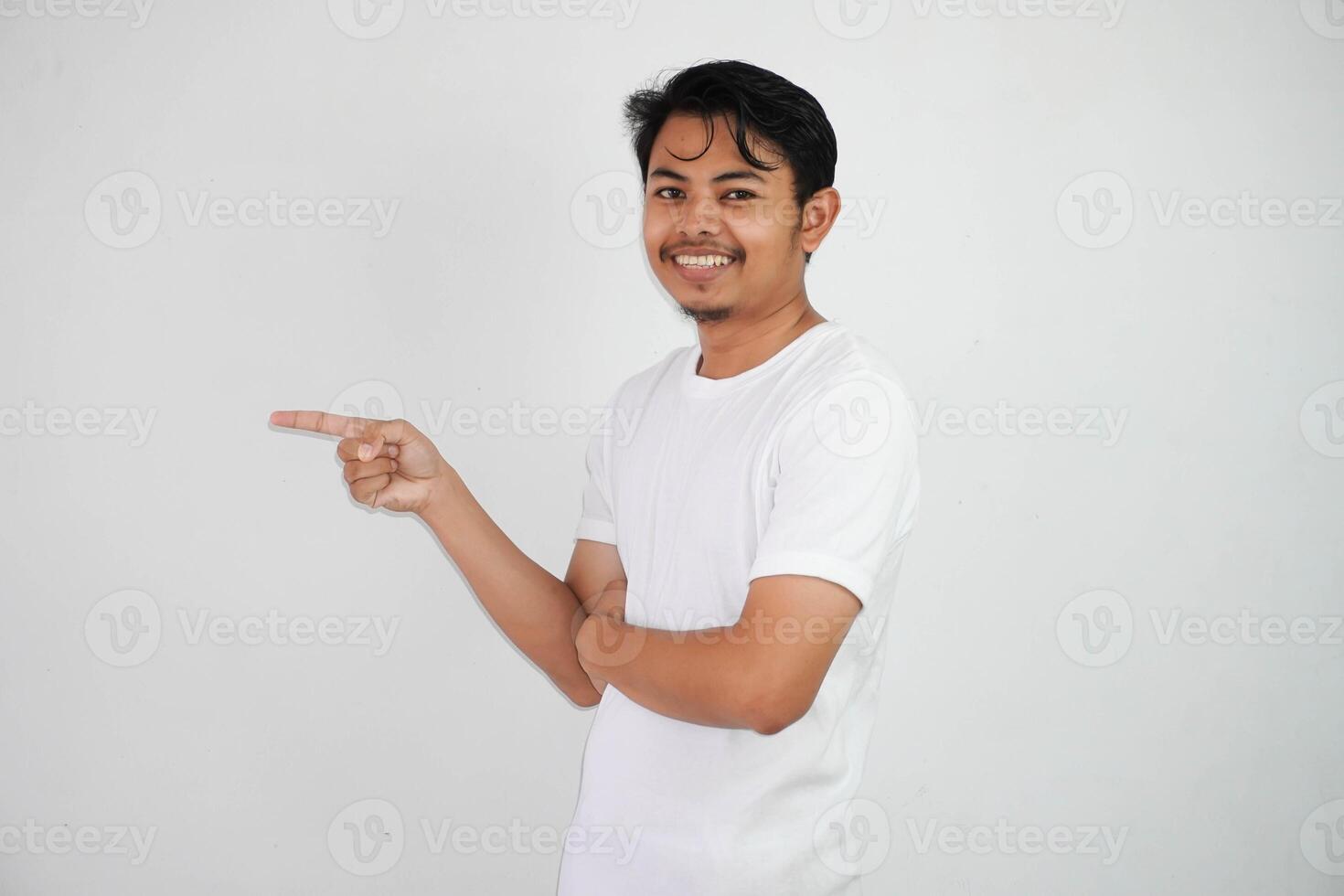 sorridente asiatico uomo con dita puntamento per il lato indossare bianca t camicia isolato su bianca sfondo foto