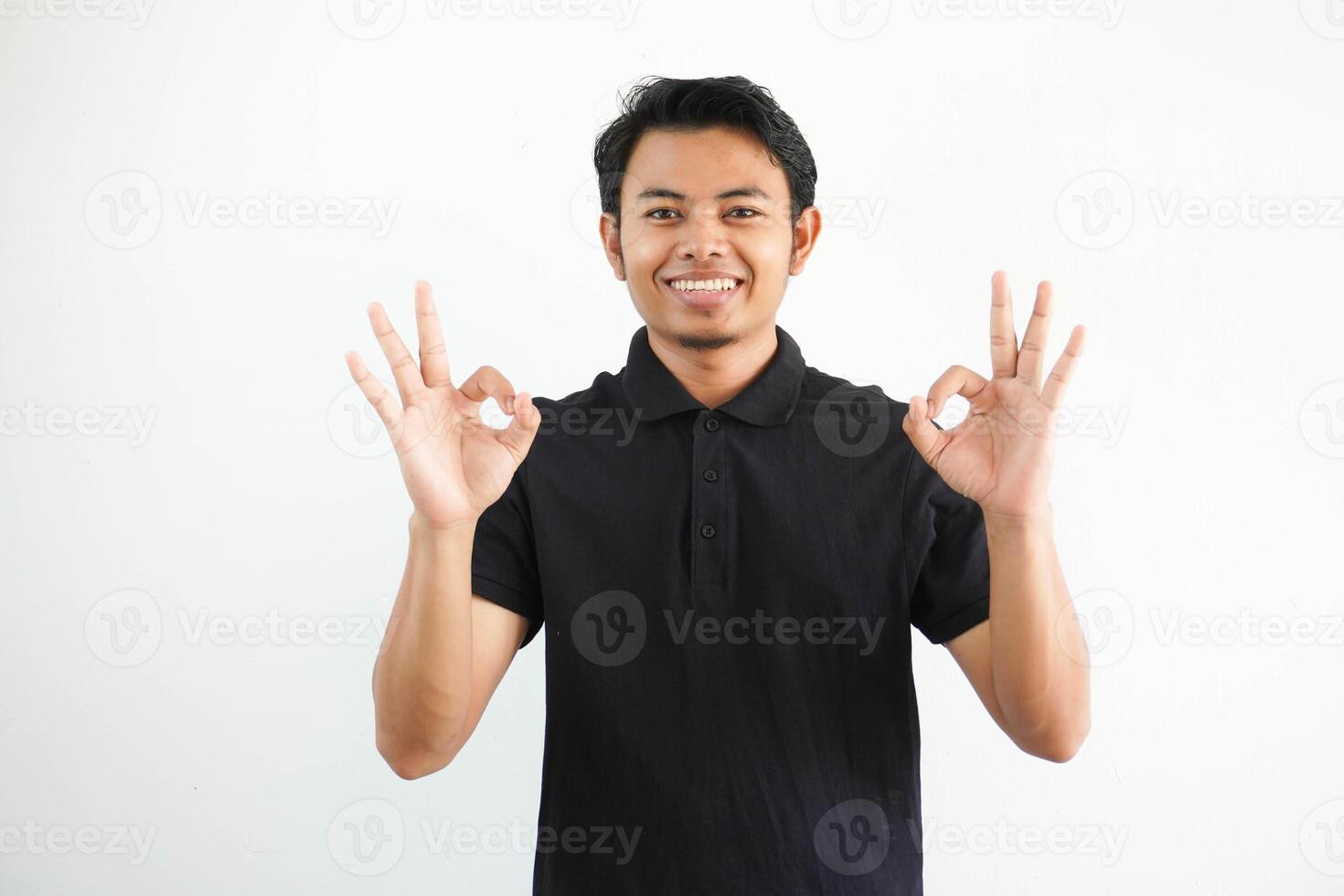 giovane asiatico uomo sorridente amichevole mentre dando ok dito cartello indossare nero polo t camicia isolato su bianca sfondo foto