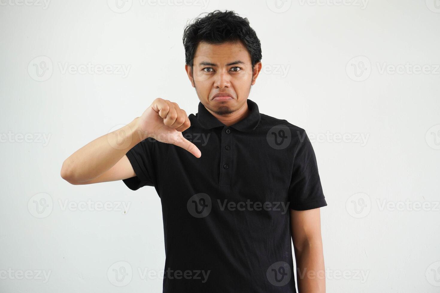 giovane asiatico uomo mostrando pollice giù cartello con negativo espressione indossare nero polo t camicia isolato su bianca sfondo foto