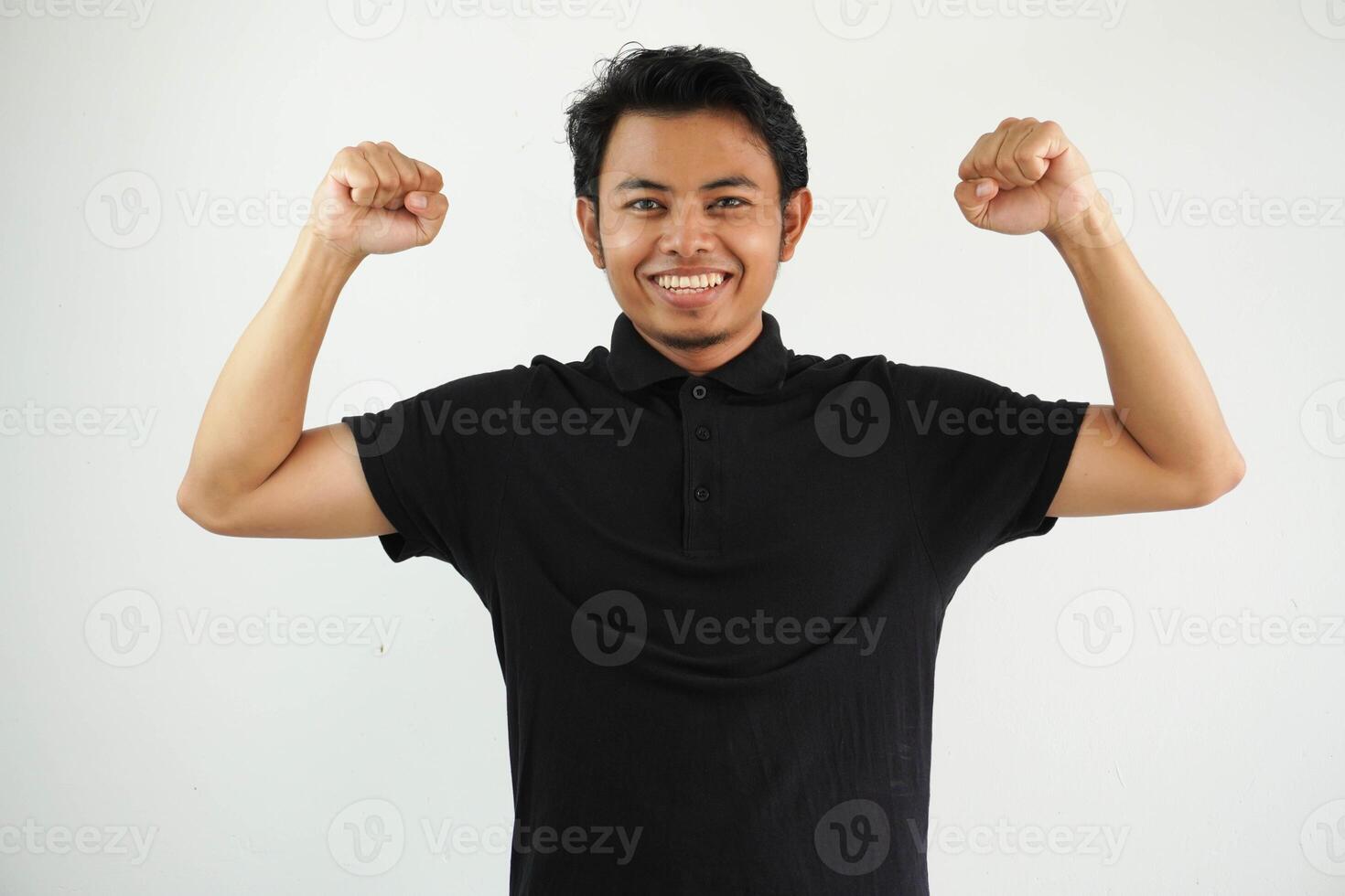 giovane asiatico uomo contro un' vivace bianca studio sfondo, mostrando forza gesto con braccia, simbolo di energia indossare nero polo t camicia. foto