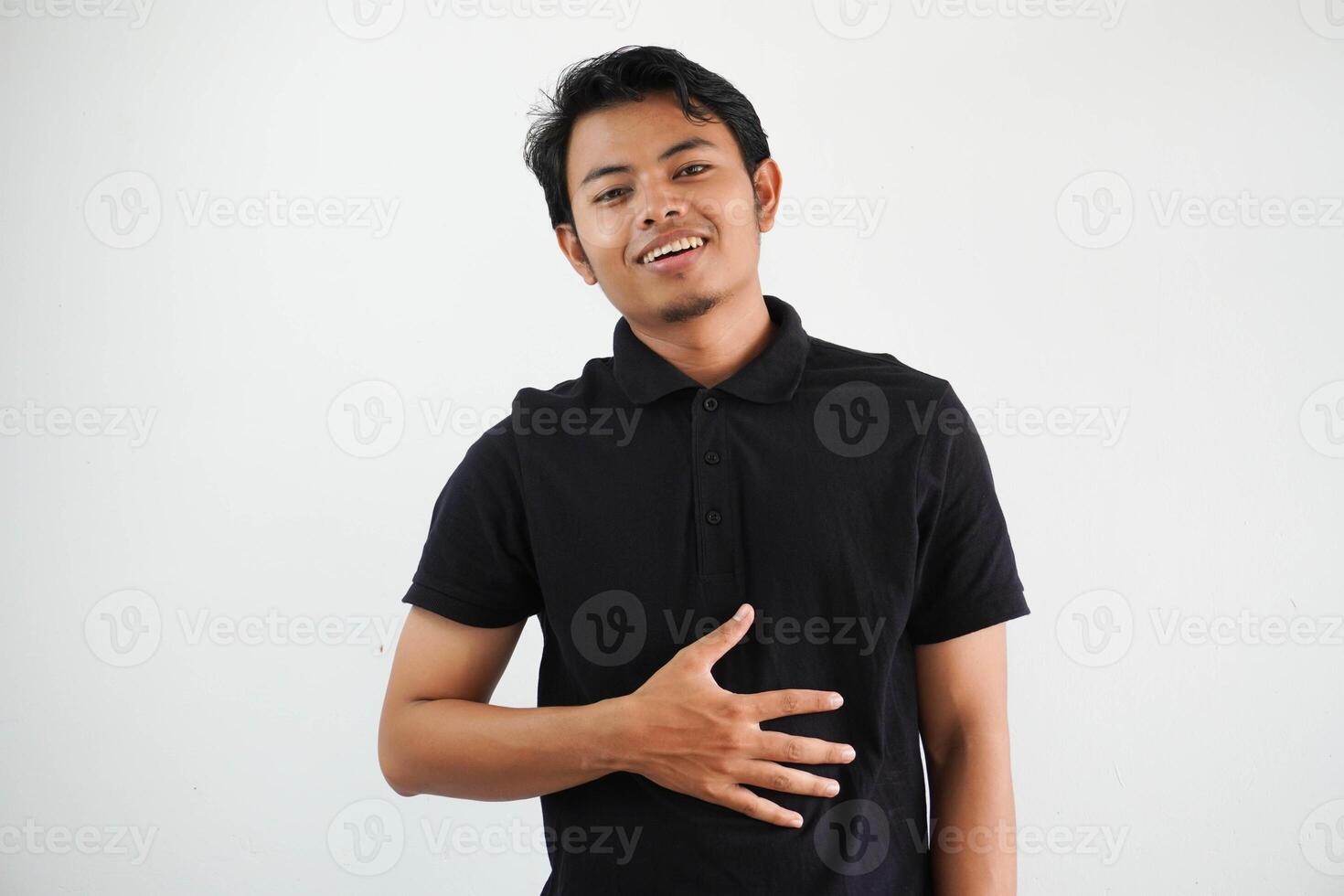 giovane asiatico uomo in posa su un' bianca fondale indossare nero polo t camicia tocchi pancia, sorrisi delicatamente, mangiare e soddisfazione concetto. foto