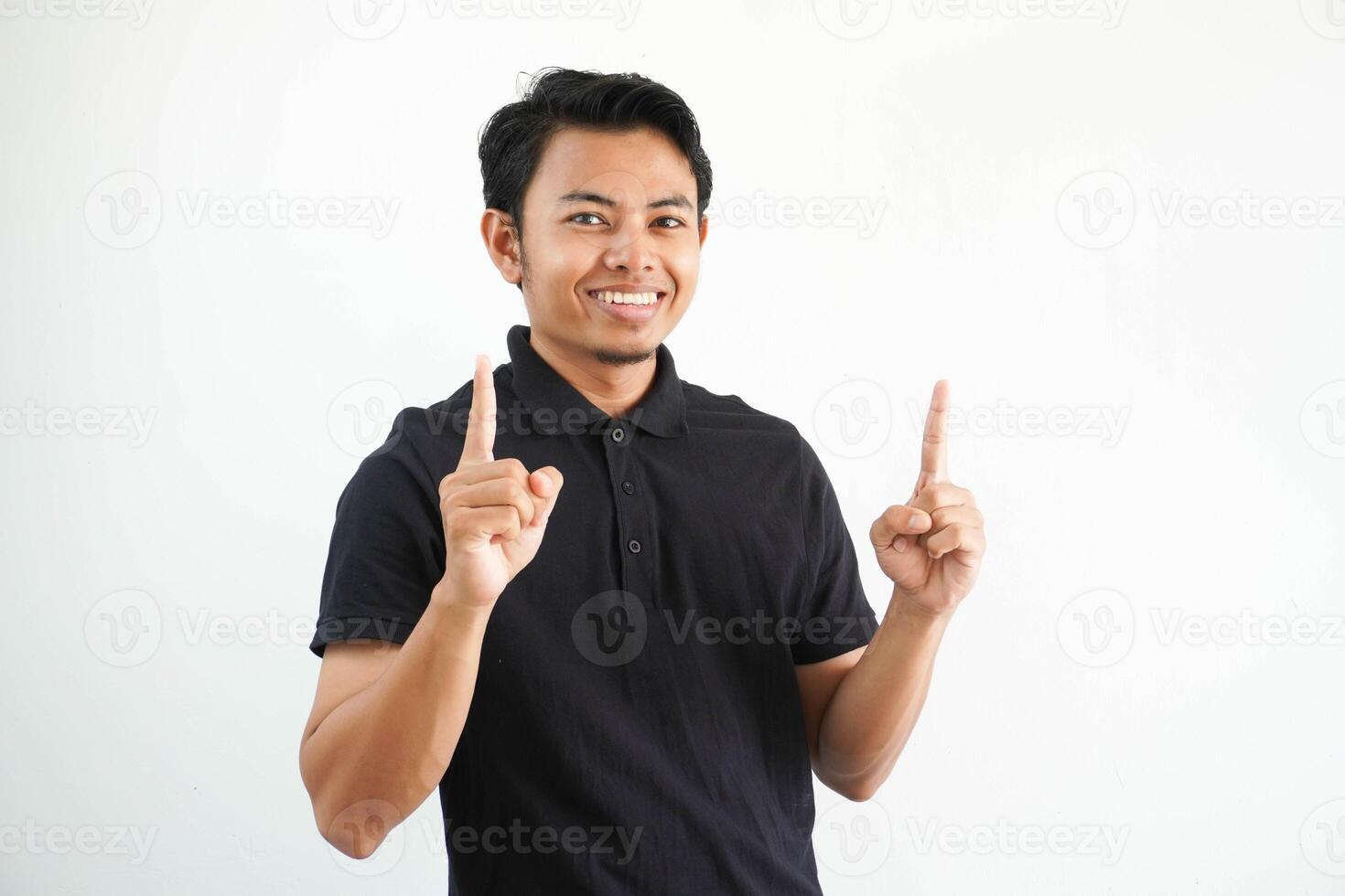 giovane asiatico uomo sorridente contento e puntamento tutti e due mani su indossare nero polo t camicia isolato su bianca sfondo foto