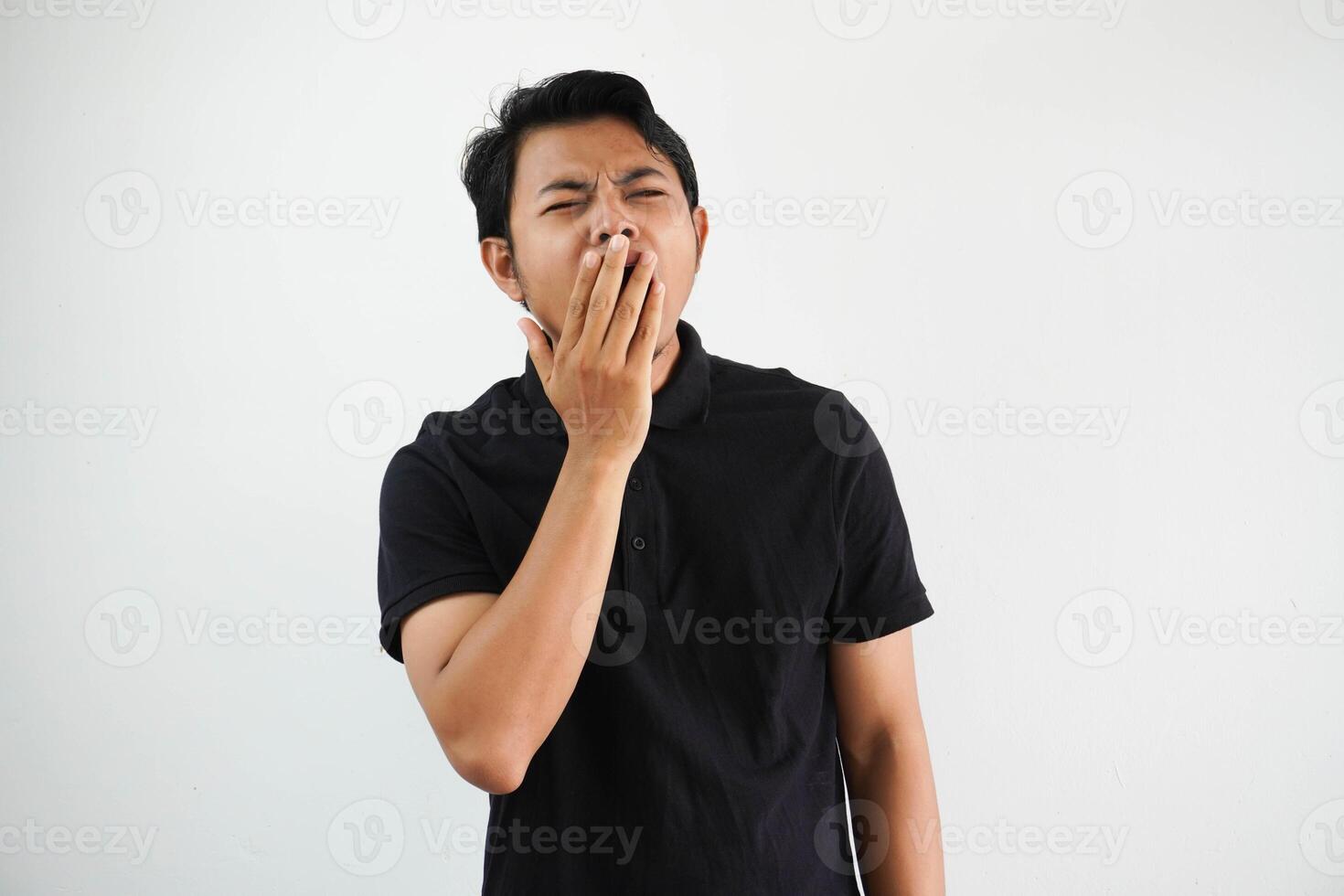 assonnato giovane asiatico uomo sbadigli di copertura bocca con mano indossare nero polo t camicia isolato su bianca sfondo foto