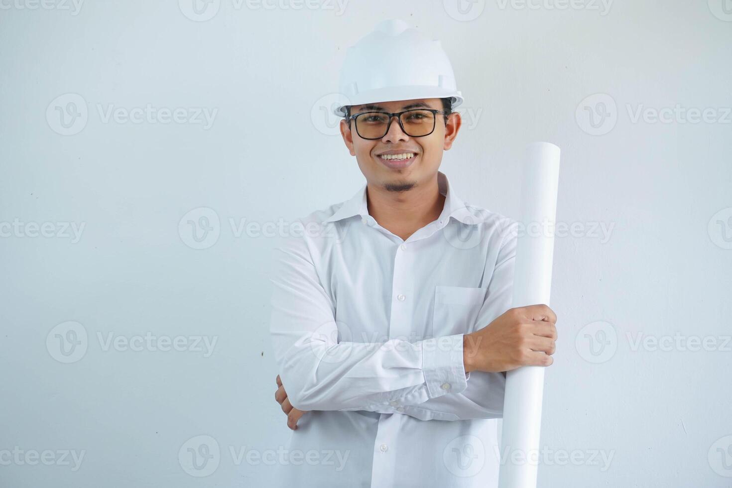 giovane asiatico uomo è ingegnere indossare casco in piedi con Tenere progetto carta Piano e sorridente con fiducioso, architetto o contraente, lavoratore o lavoro duro e faticoso, industriale concetto. foto