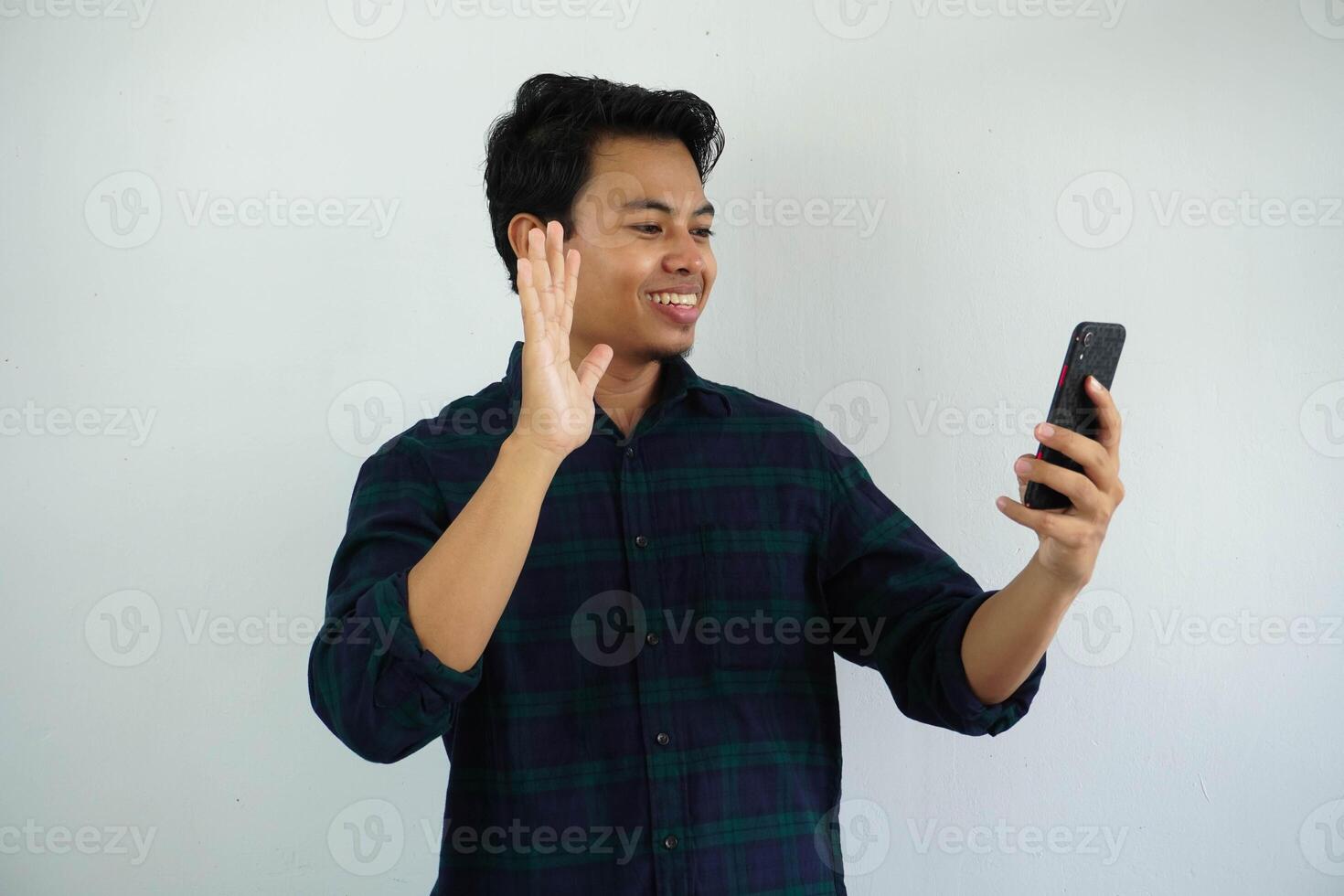 sorridente giovane asiatico uomo agitando mano con contento viso quando fare video chiamata con qualcuno isolato su bianca sfondo. foto