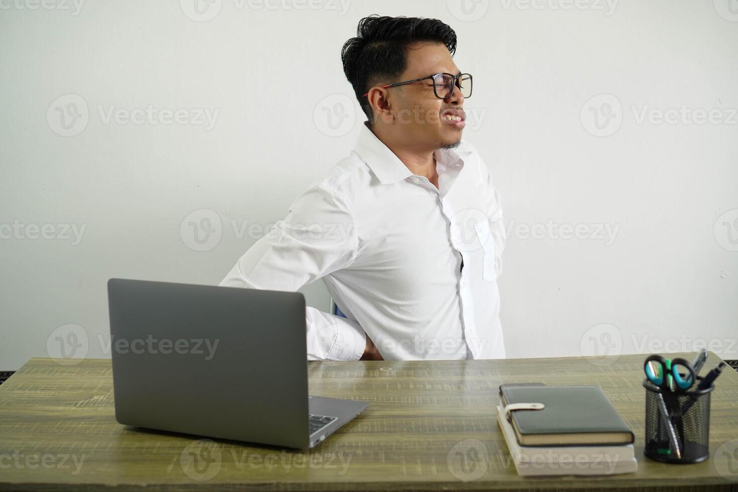 giovane asiatico uomo d'affari nel un' posto di lavoro sofferenza a partire dal mal di schiena per avendo fatto un sforzo indossare bianca camicia con bicchieri isolato foto