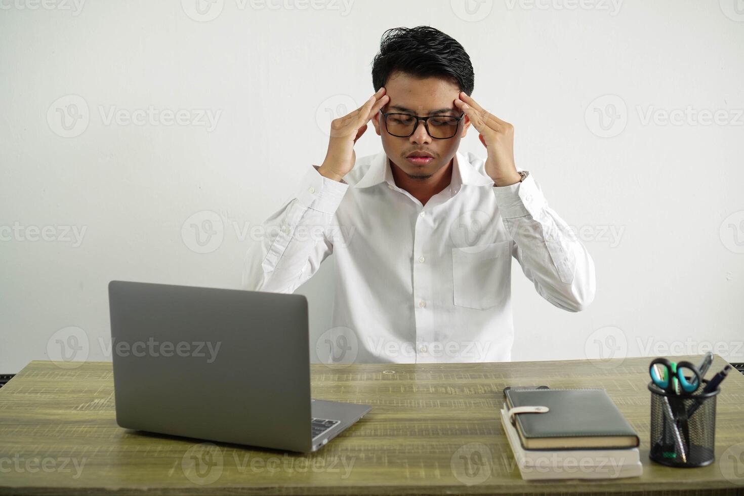 giovane asiatico uomo d'affari nel un' posto di lavoro con male alla testa, indossare bianca camicia con bicchieri isolato foto