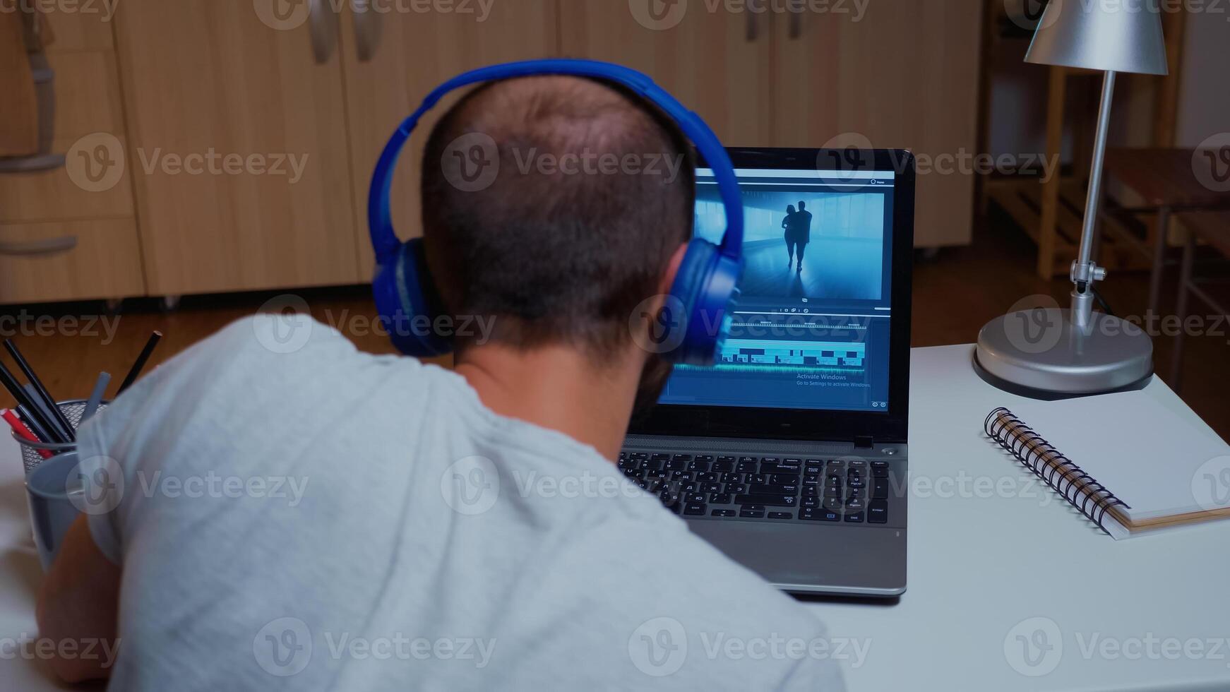 uomo Lavorando con video metraggio su il computer portatile utilizzando moderno Software. operatore video la modifica Audio film montaggio su professionale il computer portatile seduta su scrivania nel moderno cucina nel mezzanotte foto