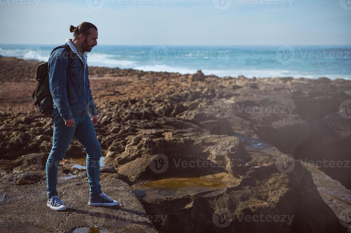 rilassato giovane adulto zaino in spalla viaggiatore avventuriero in piedi su scogliera di atlantico oceano mentre onde rottura su il roccia foto