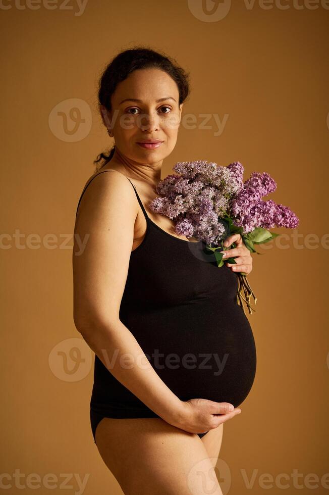 fiducioso positivo incinta donna nel nero body, in posa guardare a il telecamera, isolato su beige studio sfondo foto