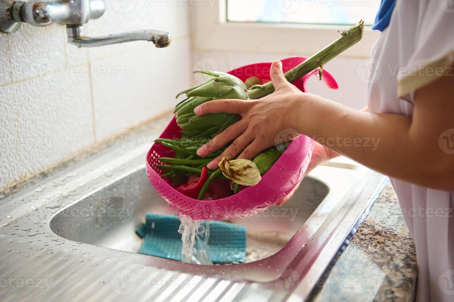 avvicinamento di femmina mani lavaggio carciofo e verdure sotto fluente acqua, in piedi di un' inossidabile Lavello nel casa cucina foto