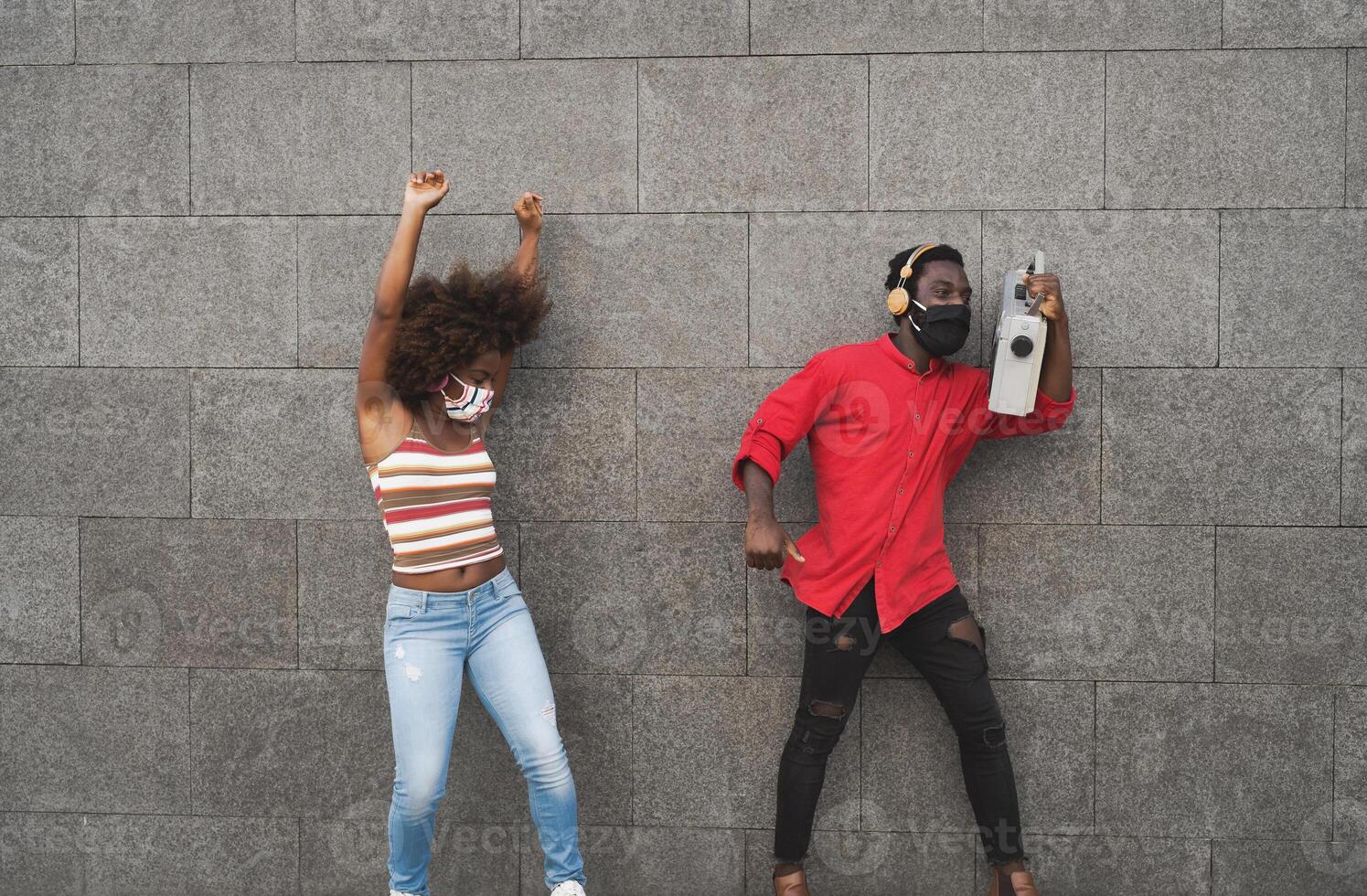 giovane africano persone indossare viso maschera e danza all'aperto mentre ascoltando per musica con senza fili cuffie e Vintage ▾ Boombox foto