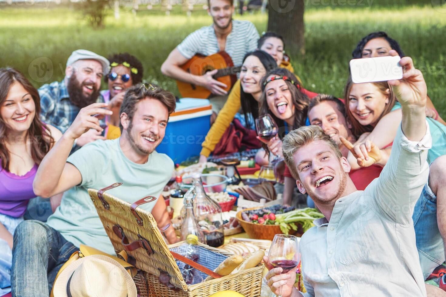 gruppo di diverso amici assunzione foto autoscatto mentre fare picnic nel parco - contento giovane persone avendo con nuovo mobile Telefono tecnologia e mangiare all'aperto - del Millennio, amicizia, cibo e bevanda concetto