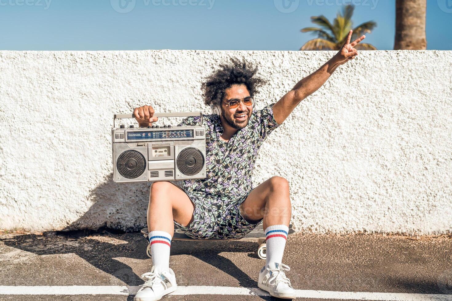 giovane afro latino uomo avendo divertimento ascoltando musica con cuffie e Vintage ▾ Boombox durante estate vacanze foto