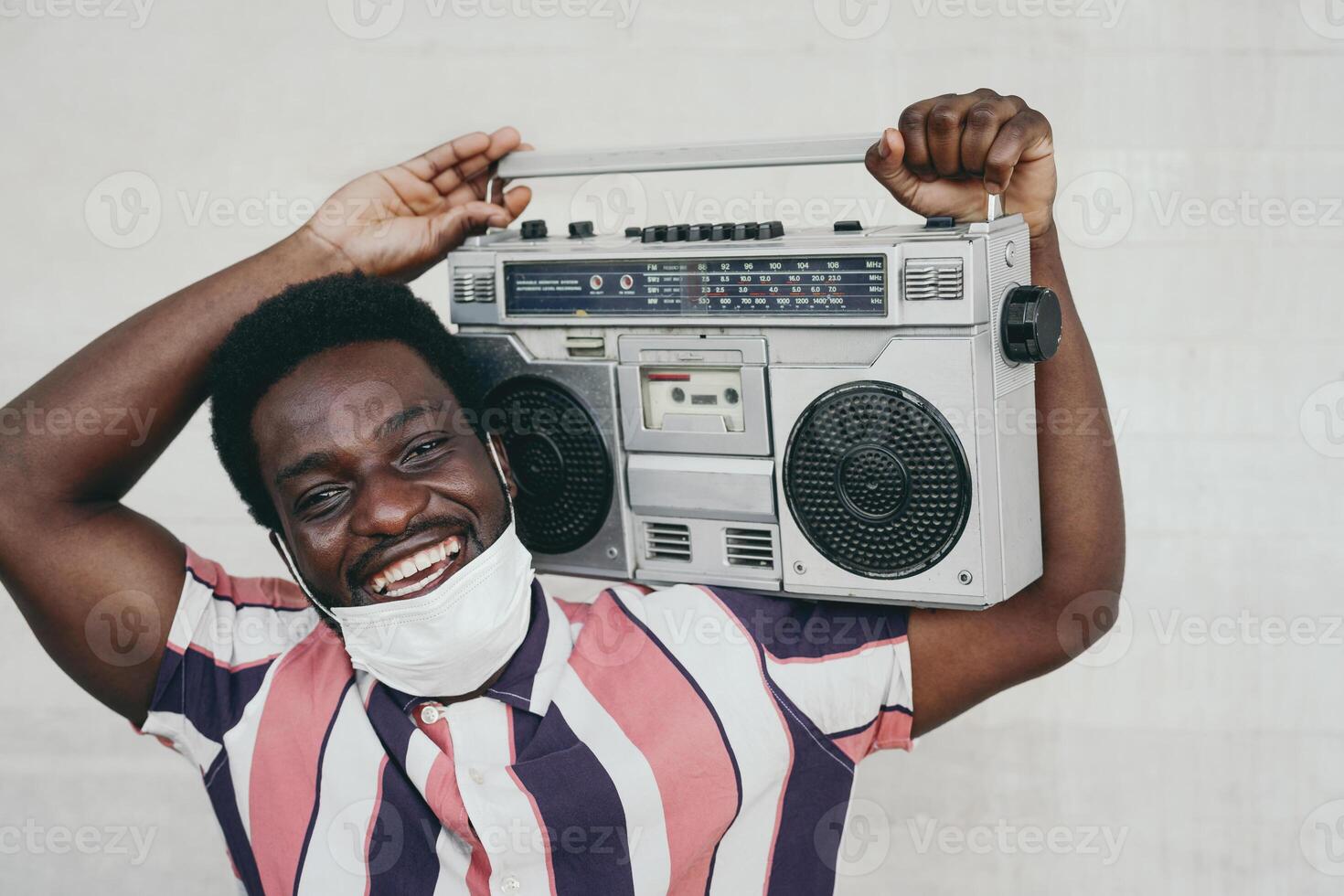 giovane africano uomo Tenere Vintage ▾ Boombox avendo divertimento all'aperto - nero uomo indossare viso maschera mentre ascoltando musica con stereo durante corona virus pandemia - gioventù persone e covid19 scoppio concetto foto