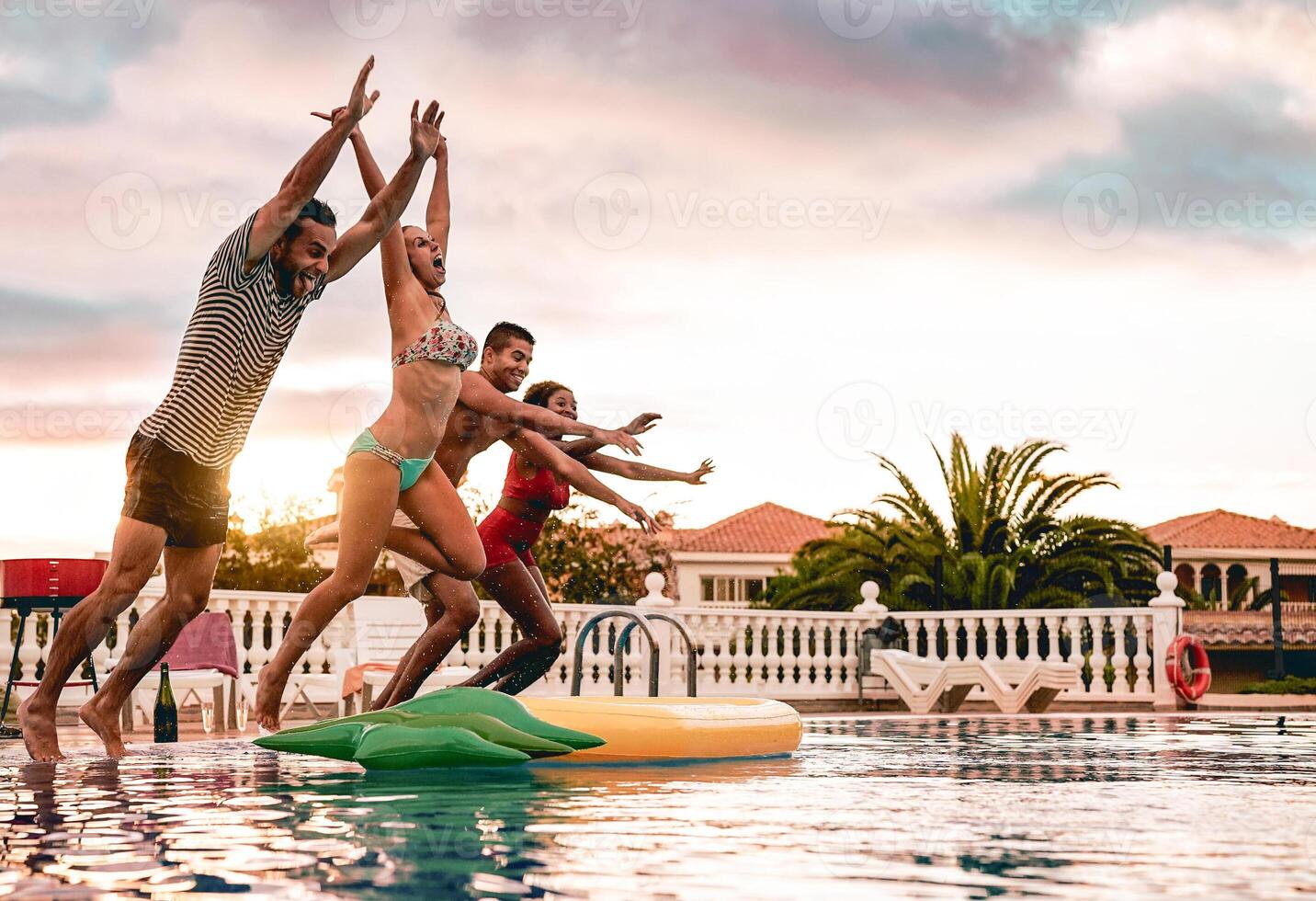 gruppo di contento amici salto nel piscina a tramonto tempo - del Millennio giovane persone avendo divertimento fabbricazione festa nel esclusivo ricorrere tropicale - vacanze, estate, vacanza e gioventù stile di vita concetto foto