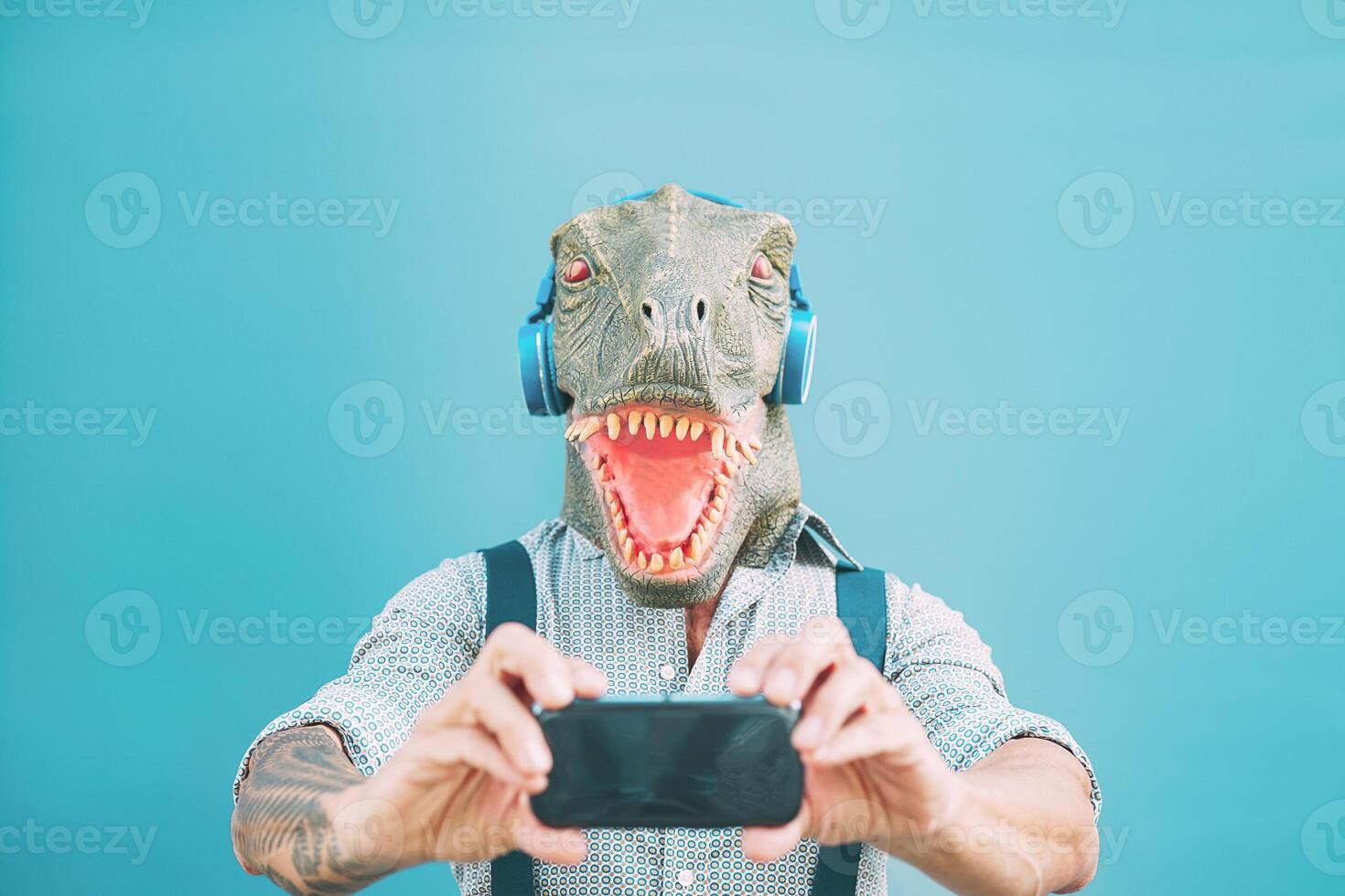 anziano moda uomo assunzione autoscatto con mobile smartphone mentre indossare t-rex maschera - fricchettone tipo avendo divertimento ascoltando musica masquerade con cuffie - divertente e assurdo surreale concetti foto