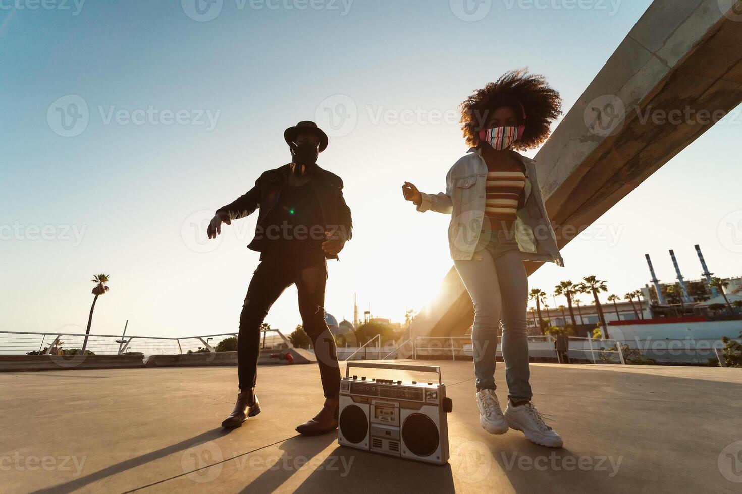 giovane afro amici indossare viso maschera danza all'aperto mentre ascoltando per musica con senza fili cuffie e Vintage ▾ Boombox foto