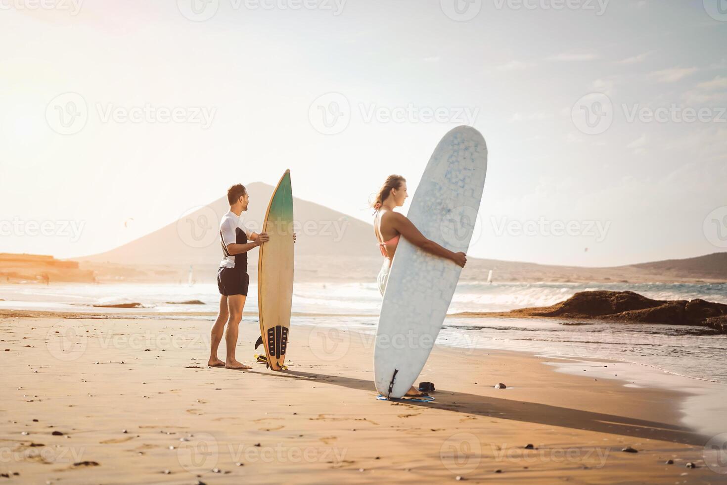 surfers coppia in piedi su il spiaggia con tavole da surf preparazione per Surf su alto onde - giovane persone avendo divertimento durante fare surf giorno - estremo Salute sport e gioventù stile di vita cultura concetto foto