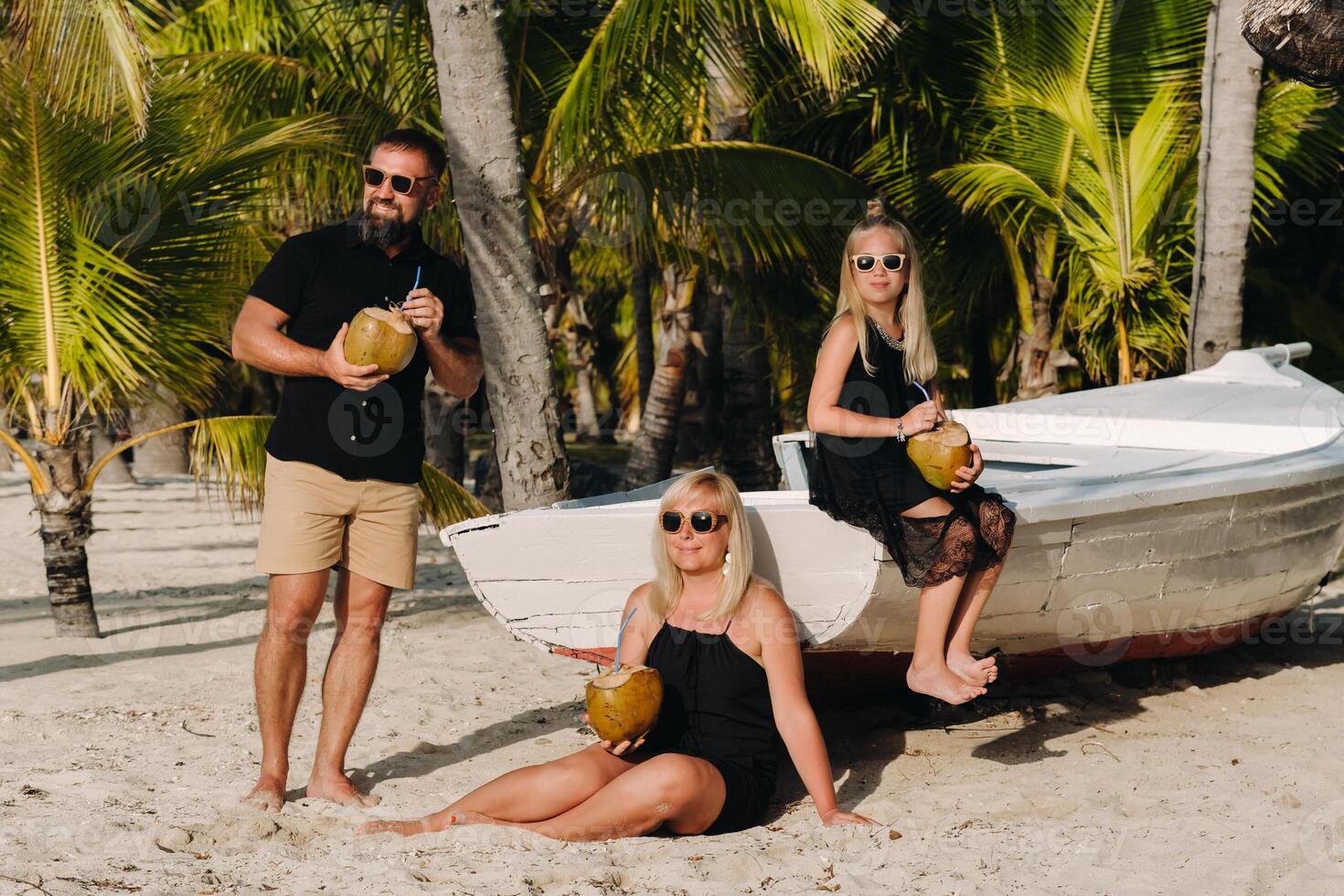 un' elegante famiglia nel nero Abiti con noci di cocco nel loro mani su il spiaggia di il isola di mauritius.bellissimo famiglia su il isola di mauritius nel il indiano oceano foto