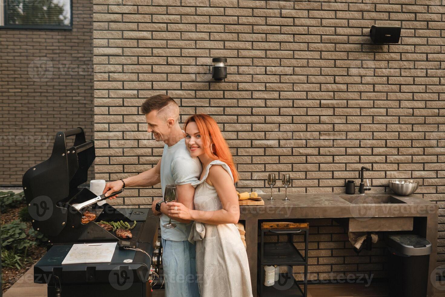 un' sposato coppia cuochi grigliato carne insieme su loro terrazza foto