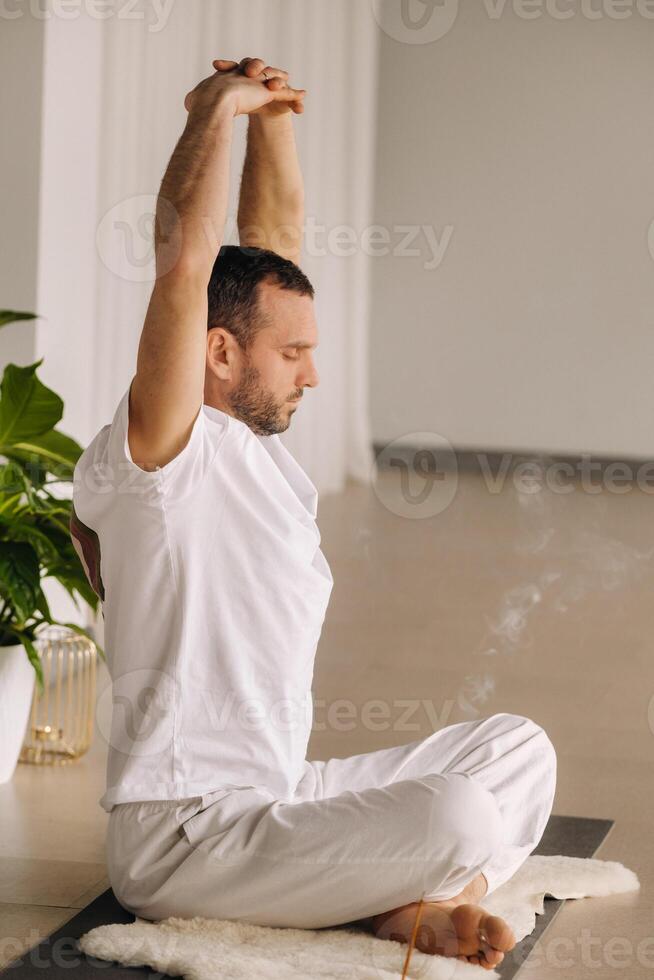 un' uomo nel bianca abbigliamento sportivo è fare yoga con un' fitness camera. il concetto di un' salutare stile di vita foto