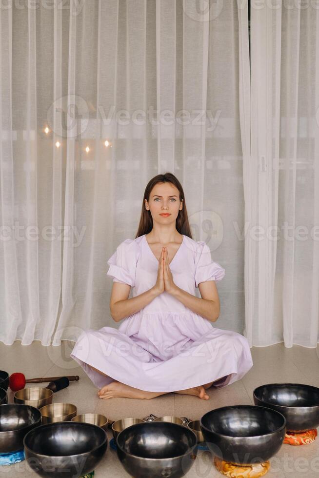 un' donna si siede con tibetano ciotole nel il loto posizione prima fare yoga nel il Palestra foto