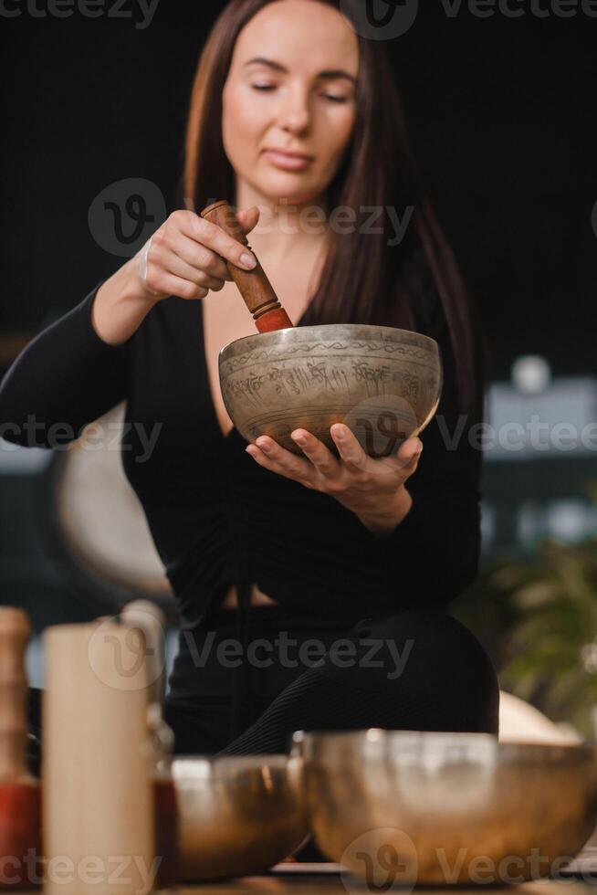 un' donna nel il loto posizione utilizzando un' cantando ciotola in casa . rilassamento e meditazione. suono terapia, alternativa medicinale. buddista guarigione pratiche foto