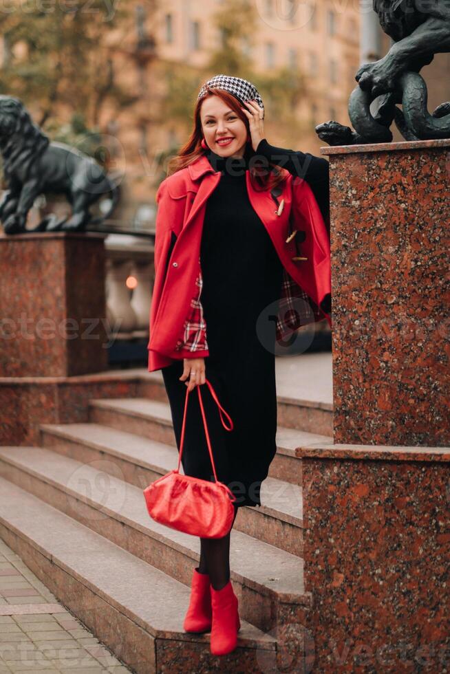 un' bellissimo elegante donna vestito nel un elegante rosso cappotto con un' elegante rosso borsetta nel il autunno città foto