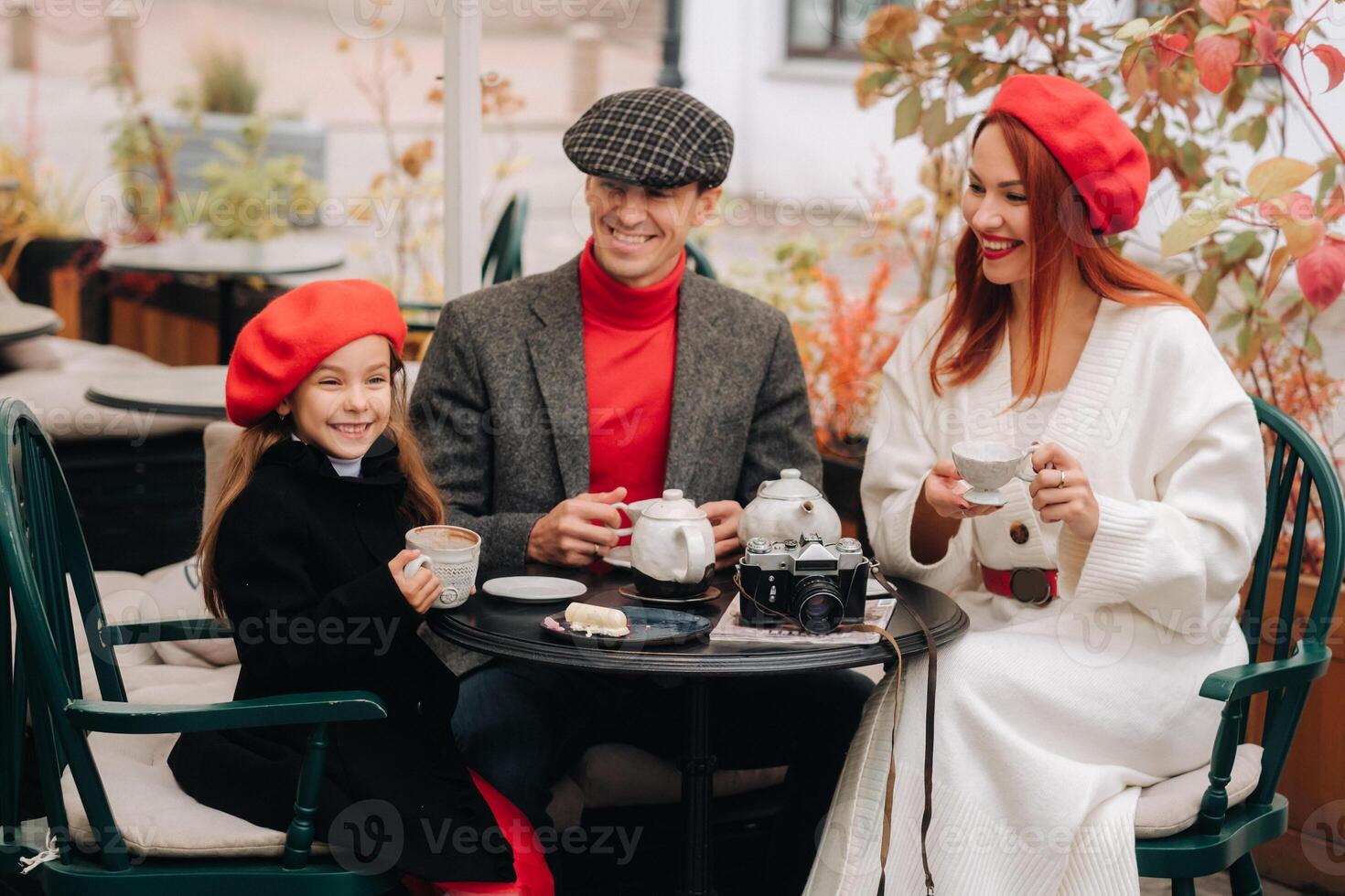 un' elegante famiglia si riunirono insieme nel un' bar su il strada. mamma, papà, poco figlia bevanda Tè, mangiare torte. essi siamo contento insieme. il concetto di un' contento famiglia cena foto