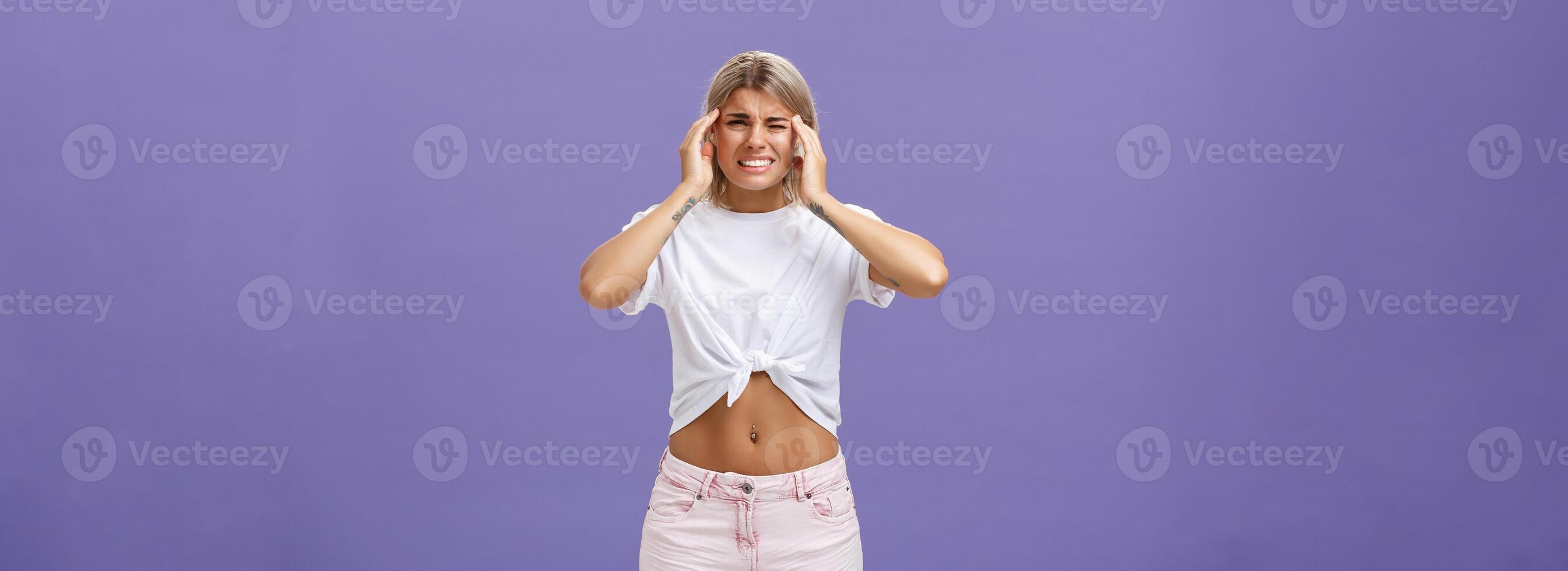 testa andando soffio a partire dal emicrania. infelice scontento attraente donna sensazione disagio sofferenza mal di testa stringendo denti accigliato Tenere dita su templi udito terribile suono al di sopra di viola parete foto