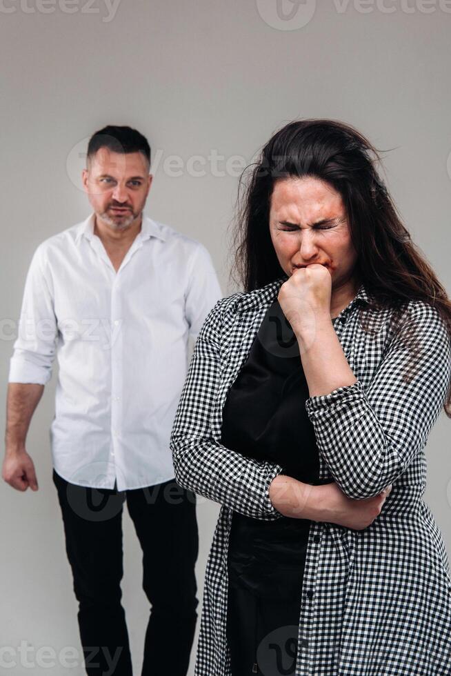 un' donna picchiato di sua marito in piedi dietro a sua e guardare a sua aggressivamente. domestico violenza foto