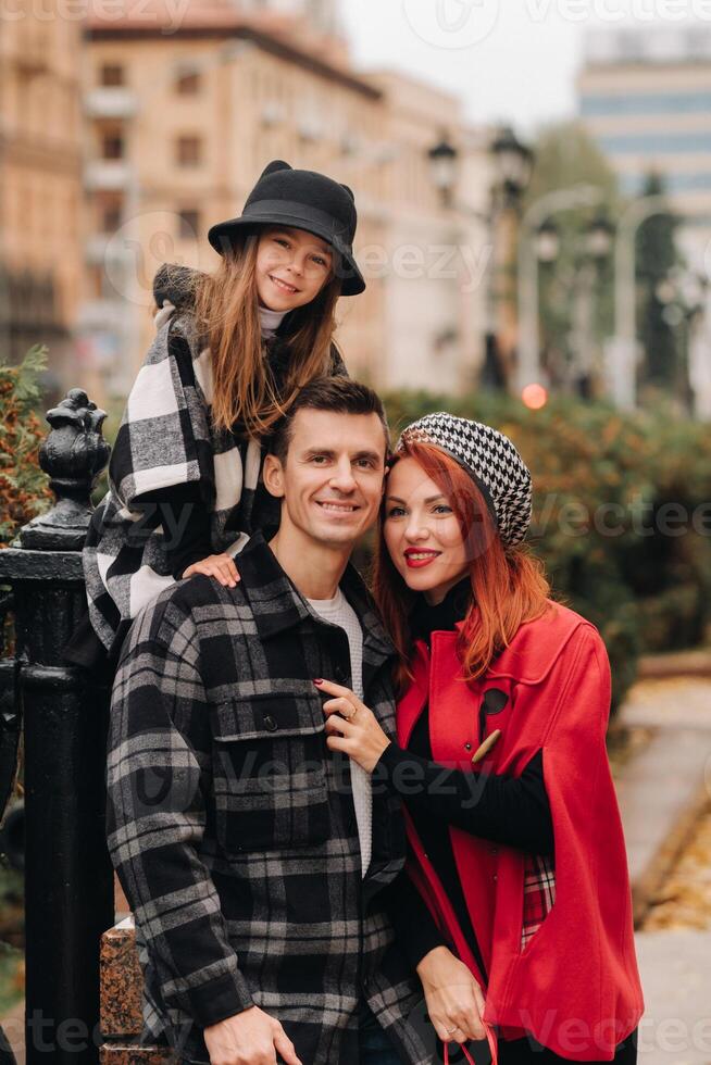 un' elegante famiglia di tre passeggiate attraverso il autunno città in posa per un' fotografo . papà, mamma e figlia nel il autunno città foto