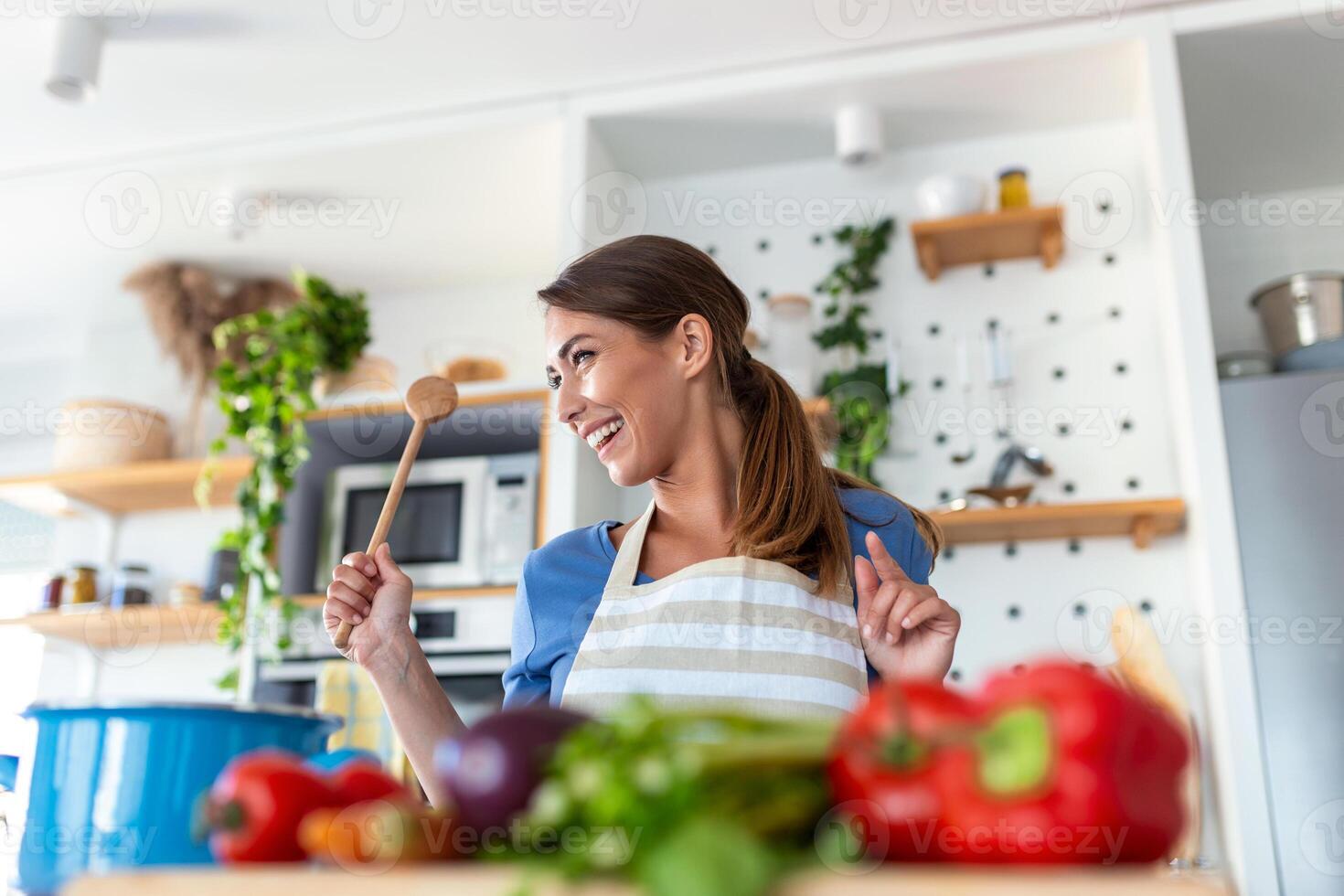 eccitato donna cantando e danza nel moderno cucina a casa, contento donna Tenere spatola come microfono, ballare, ascoltando per musica, avendo divertimento con stoviglie, preparazione prima colazione foto