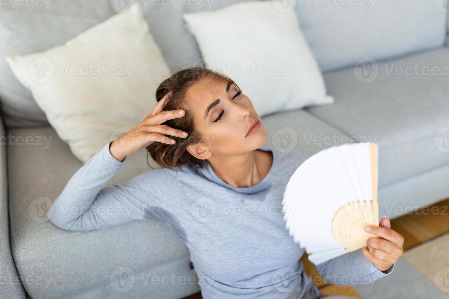 donna mette testa su divano cuscini si sente lento dovuto insopportabile calore, onde mano fan freddo se stessa, caldo estate piatto senza condizionatore clima controllo sistema concetto foto