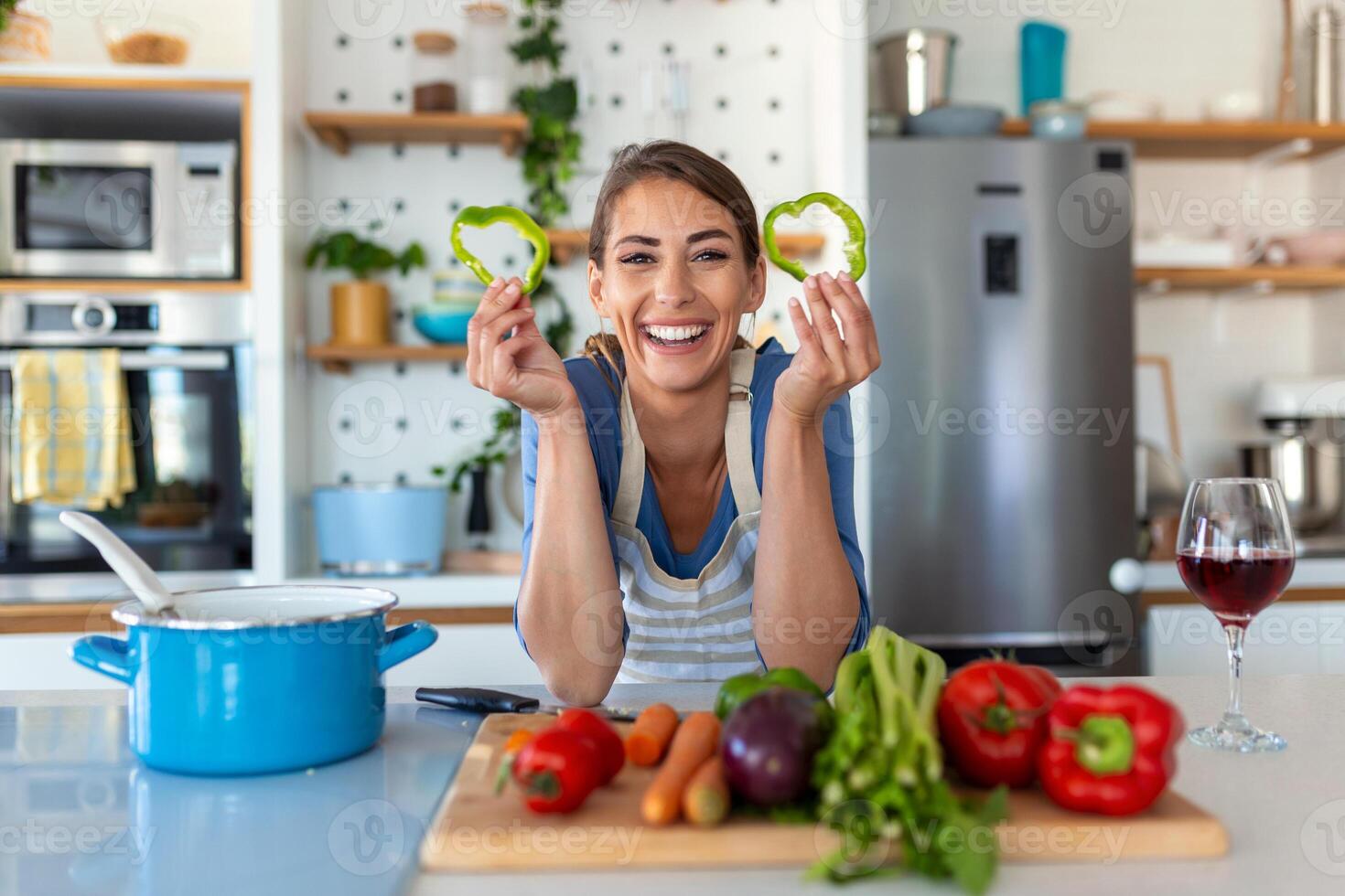 foto di giovane donna sorridente con verde Pepe fette mentre cucinando insalata con fresco verdure nel cucina interno a casa