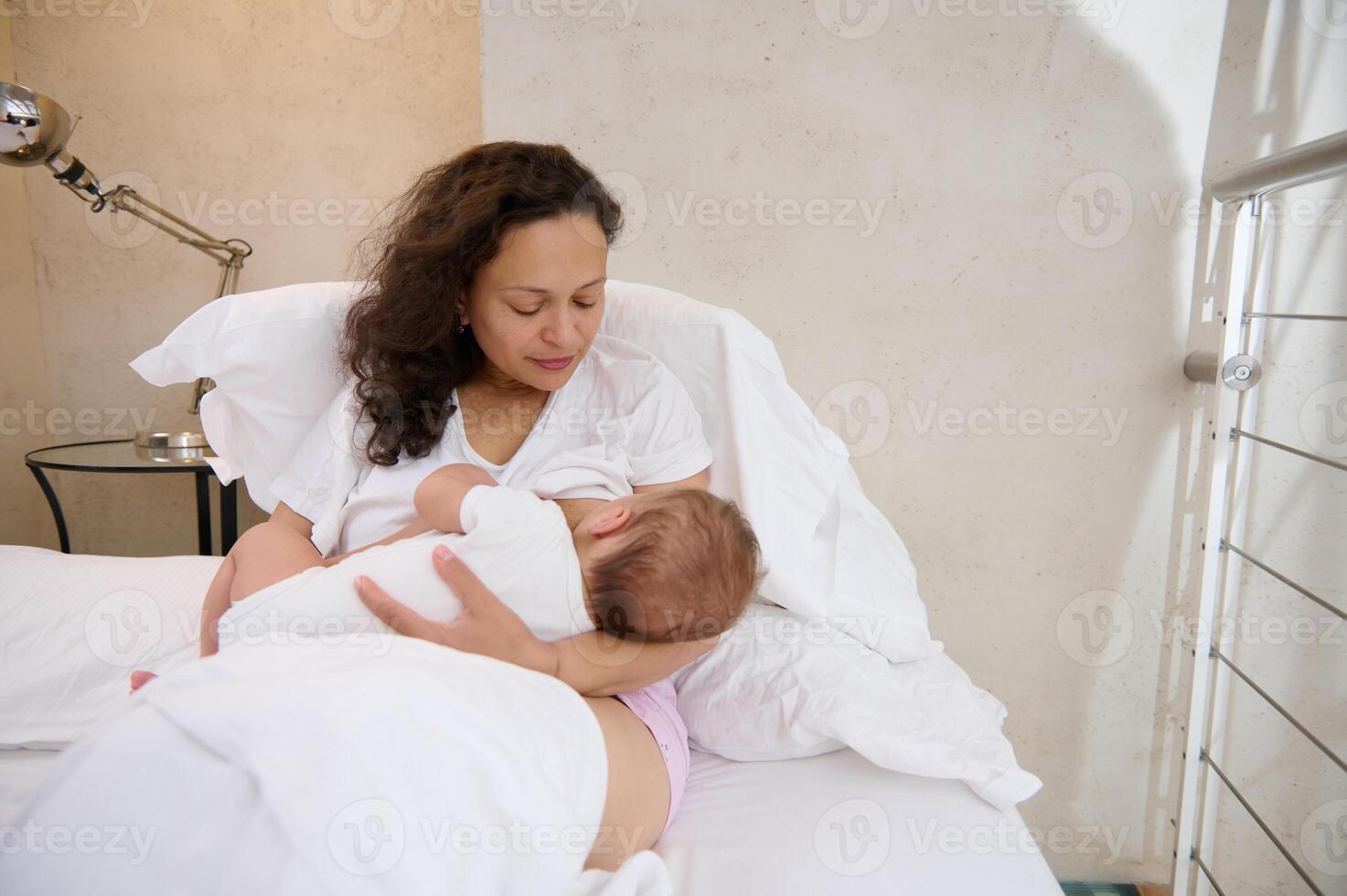 giovane madre seduta su il letto e l'allattamento al seno sua bambino. foto