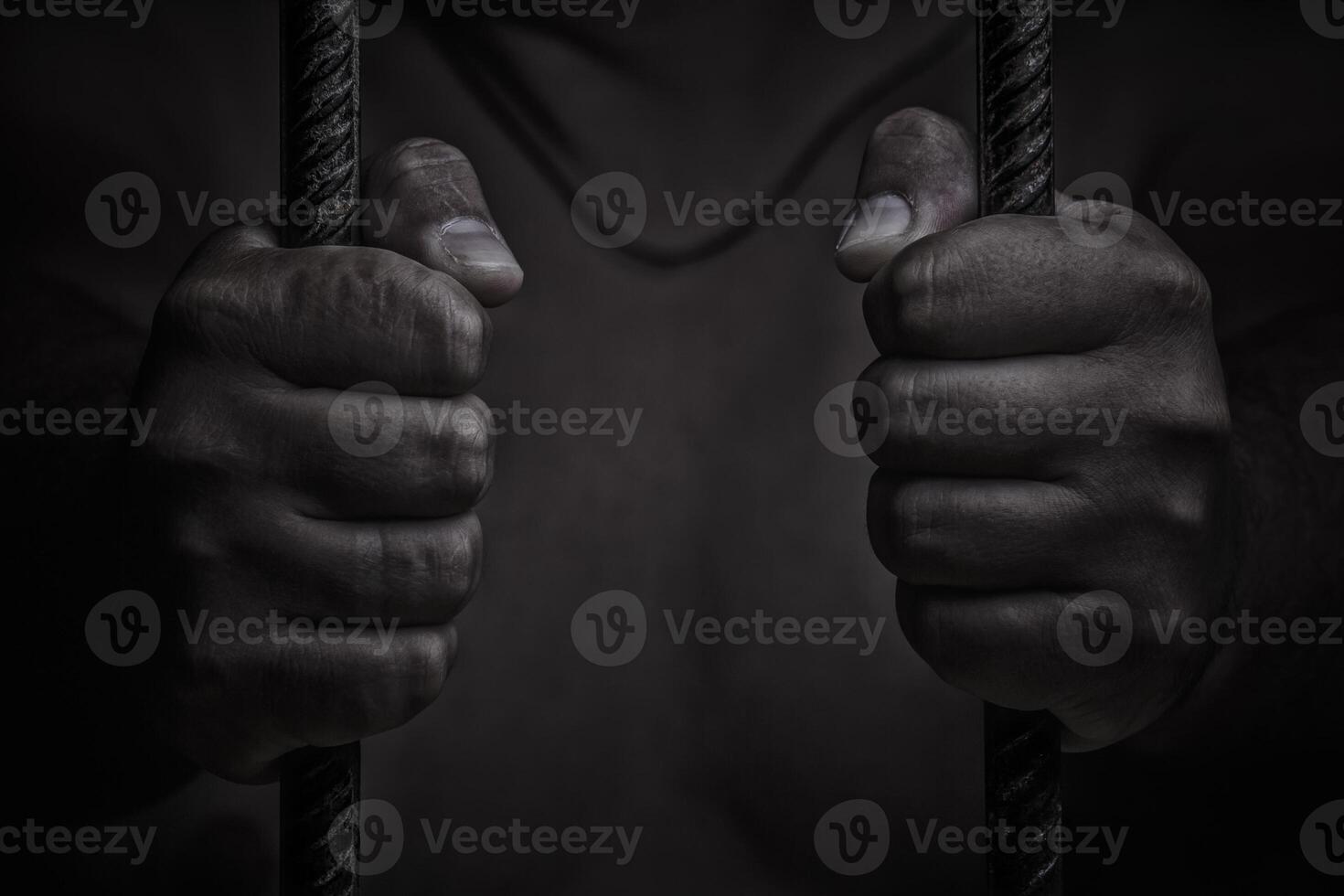 avvicinamento su mani di uomo seduta nel prigione. uomo dietro a prigione barre su nero sfondo foto