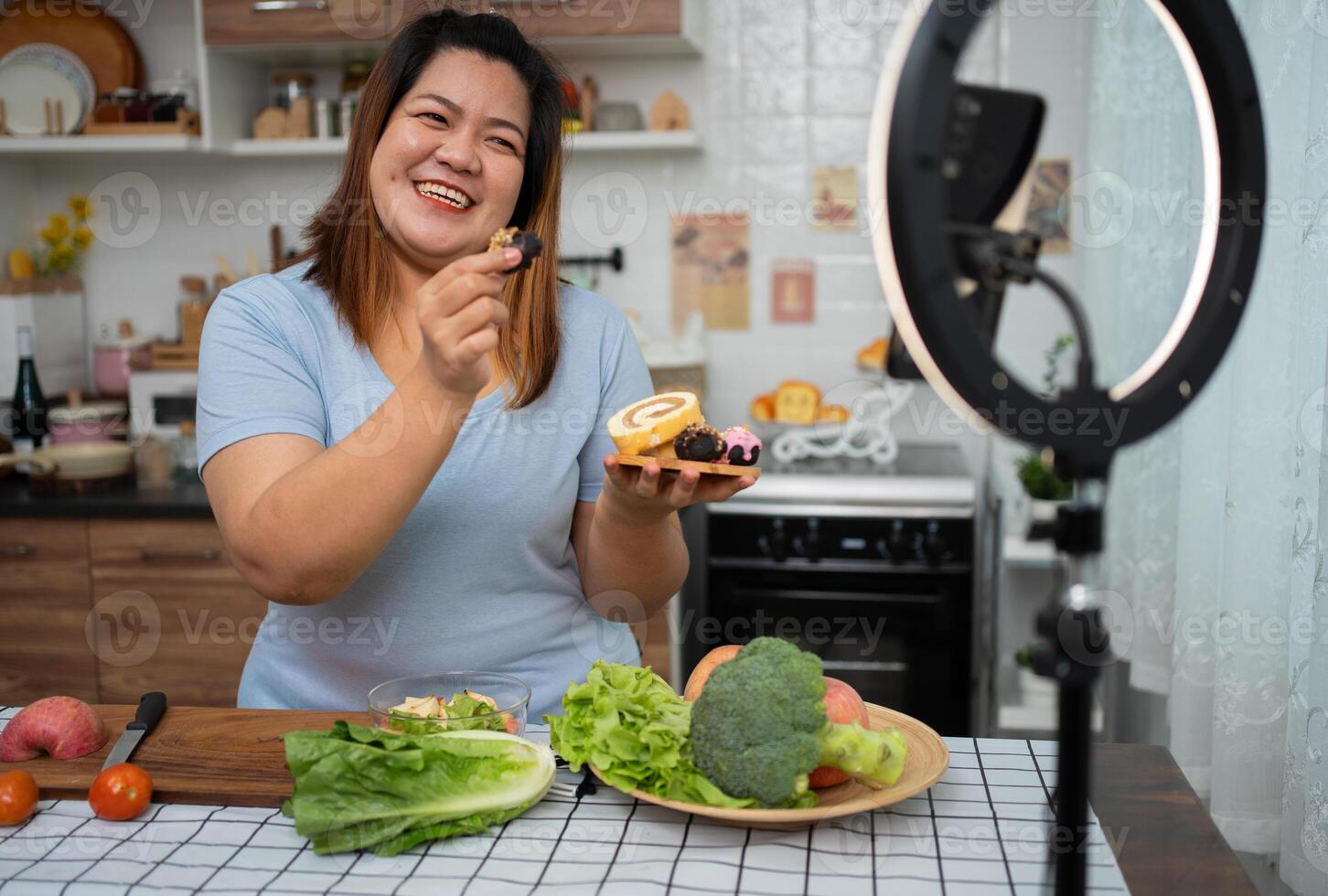 asiatico incinta blogger guardare a smartphone telecamera, lei è vivere streaming cucinando classe per incinta. asiatico donna in piedi felicemente sorridente a il cucina contatore preparazione fresco biologico insalata. foto