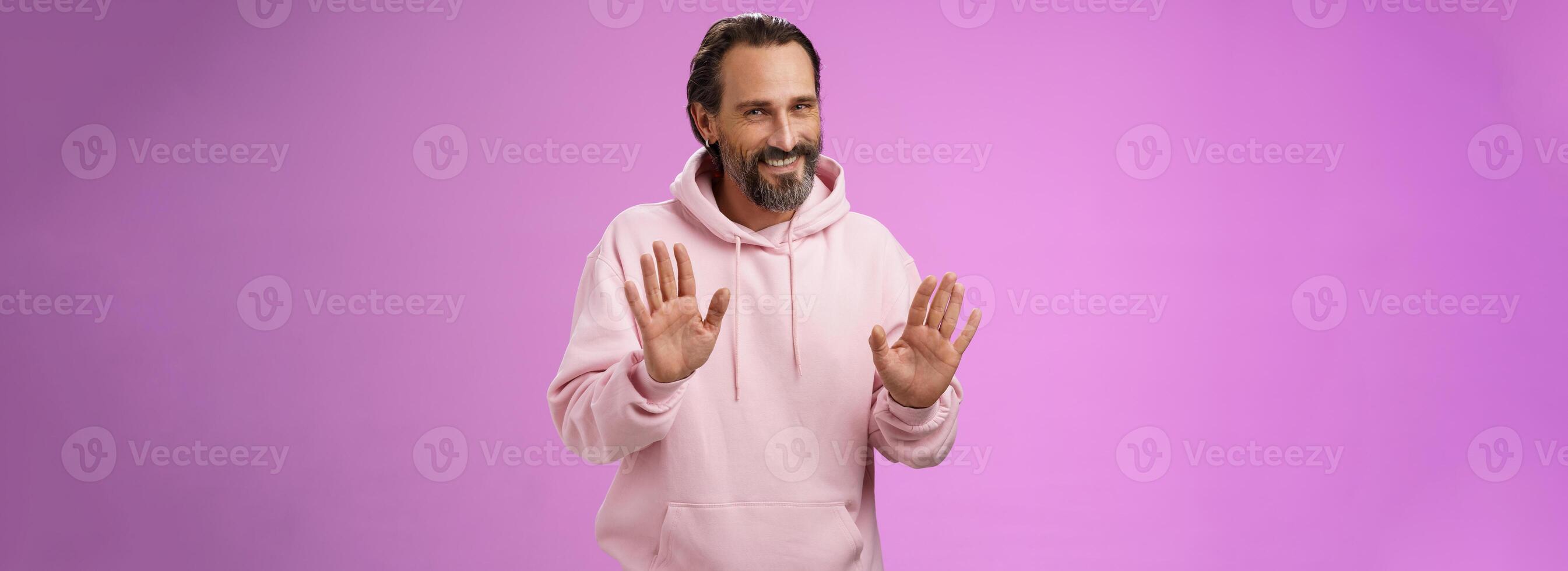 no Grazie passaggio. affascinante gentile virile adulto barbuto uomo grigio capelli nel rosa felpa con cappuccio scusandosi rifiuto aumentare palme rifiuto gesto in calo offrire sorridente dire spiacente non interessato, viola sfondo foto