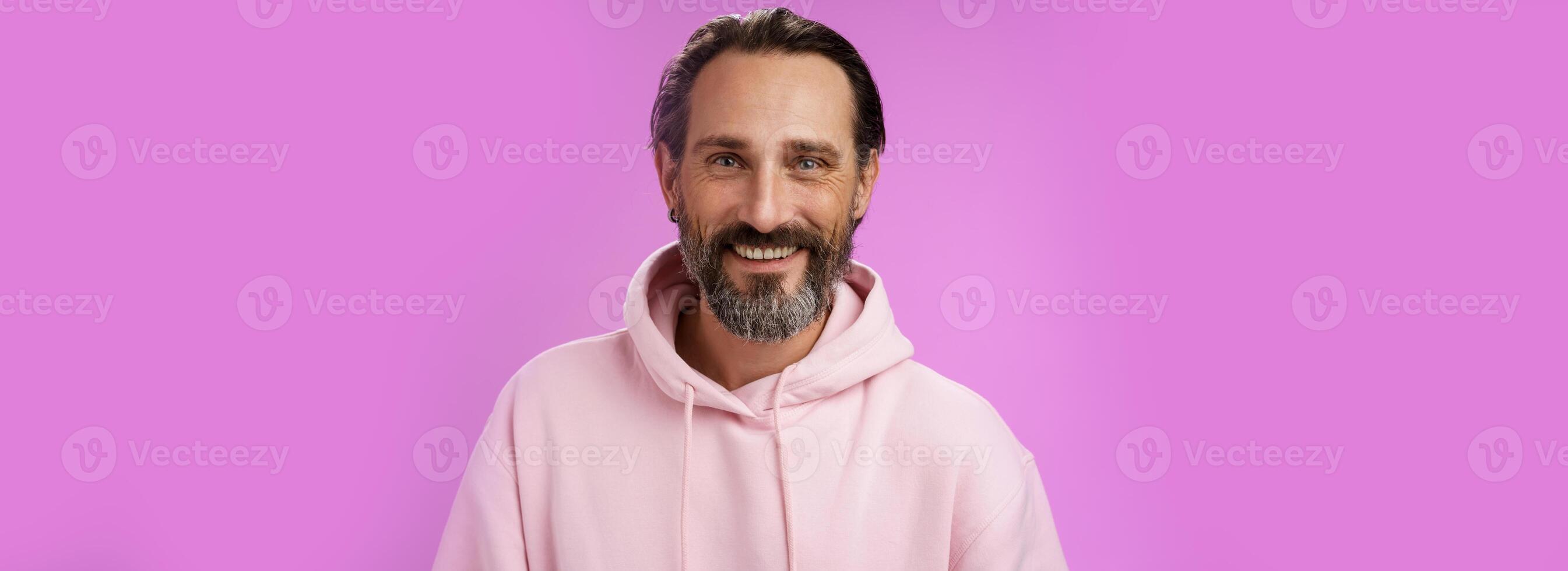 dalla vita in su contento allegro caucasico barbuto uomo grigio capelli nel rosa di moda felpa con cappuccio sorridente a grandi linee sentire salutare assistere Palestra condurre attivo stile di vita ghignante bianca Perfetto denti, in piedi viola sfondo foto